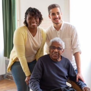 Woman, man, and older person smiling indoors; woman in yellow, man in white shirt.