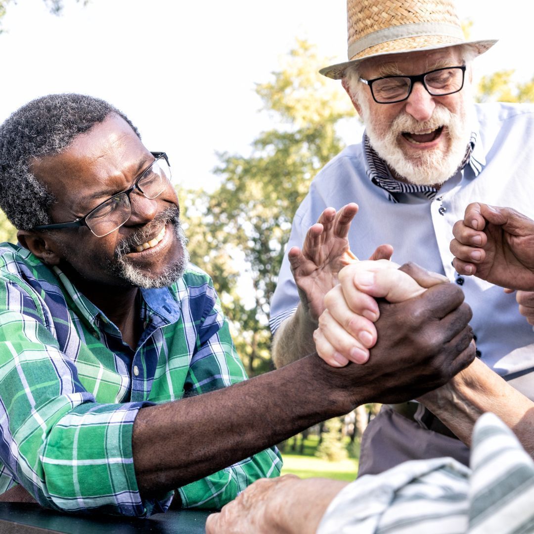 Two men arm wrestling outdoors; other men watch smiling.