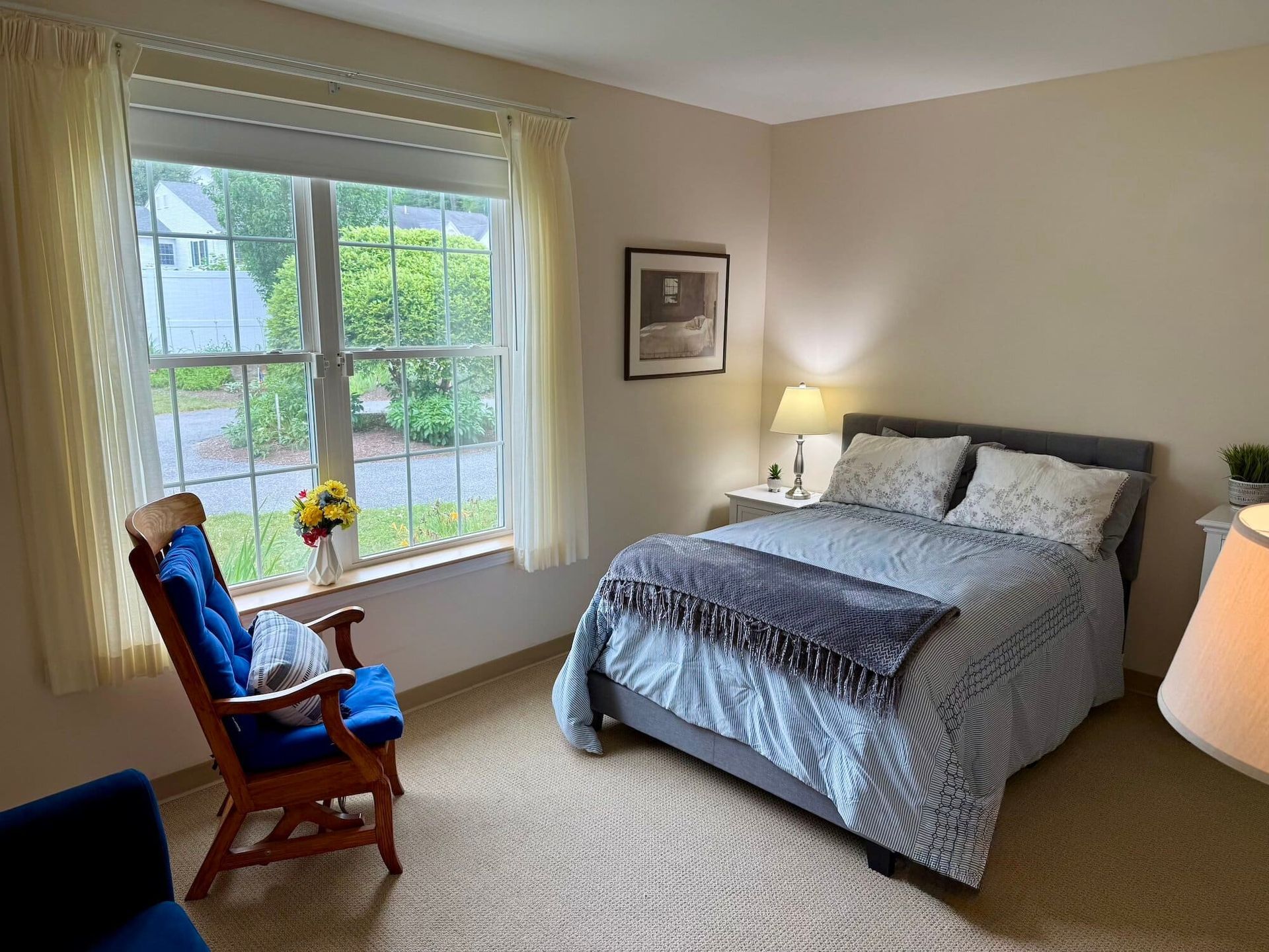 Bedroom with a window, bed, blue armchair, and a bedside table.