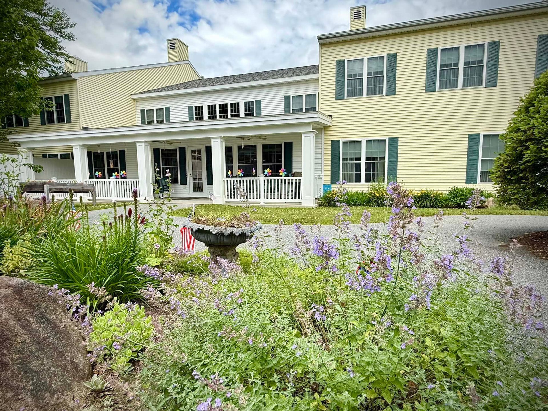 Yellow and white house with a porch and flower garden in front.