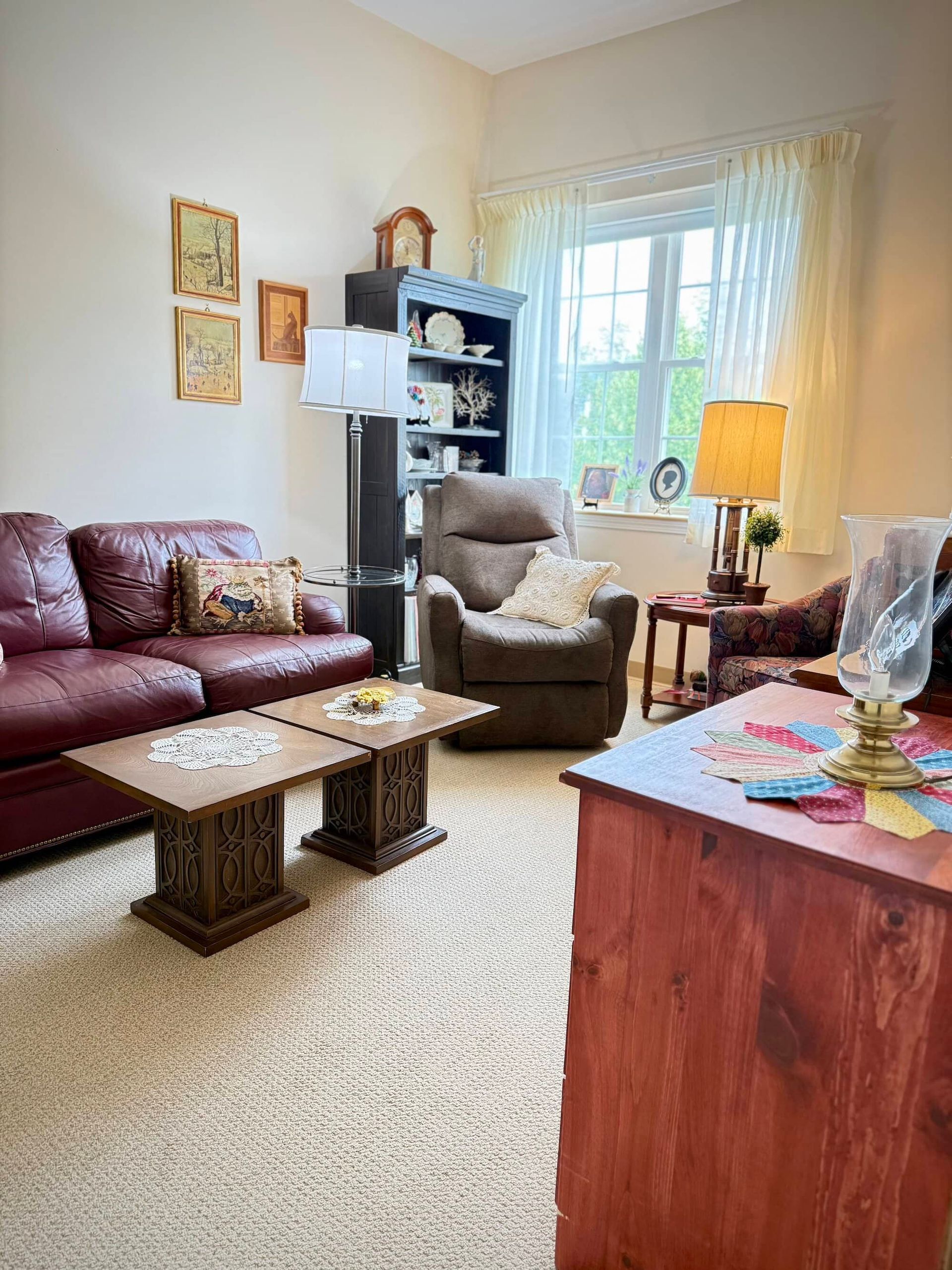 Cozy living room with burgundy sofa, recliner, and decorative coffee tables. Neutral carpet and light walls.