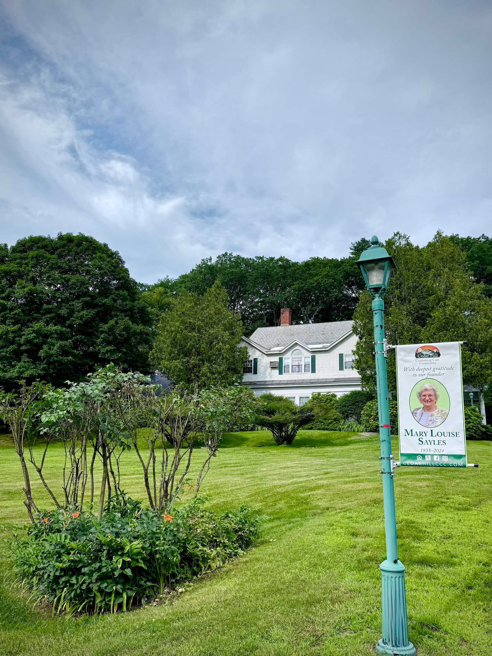 White house behind a green lawn, banner on a lamp post. Cloudy sky, trees.