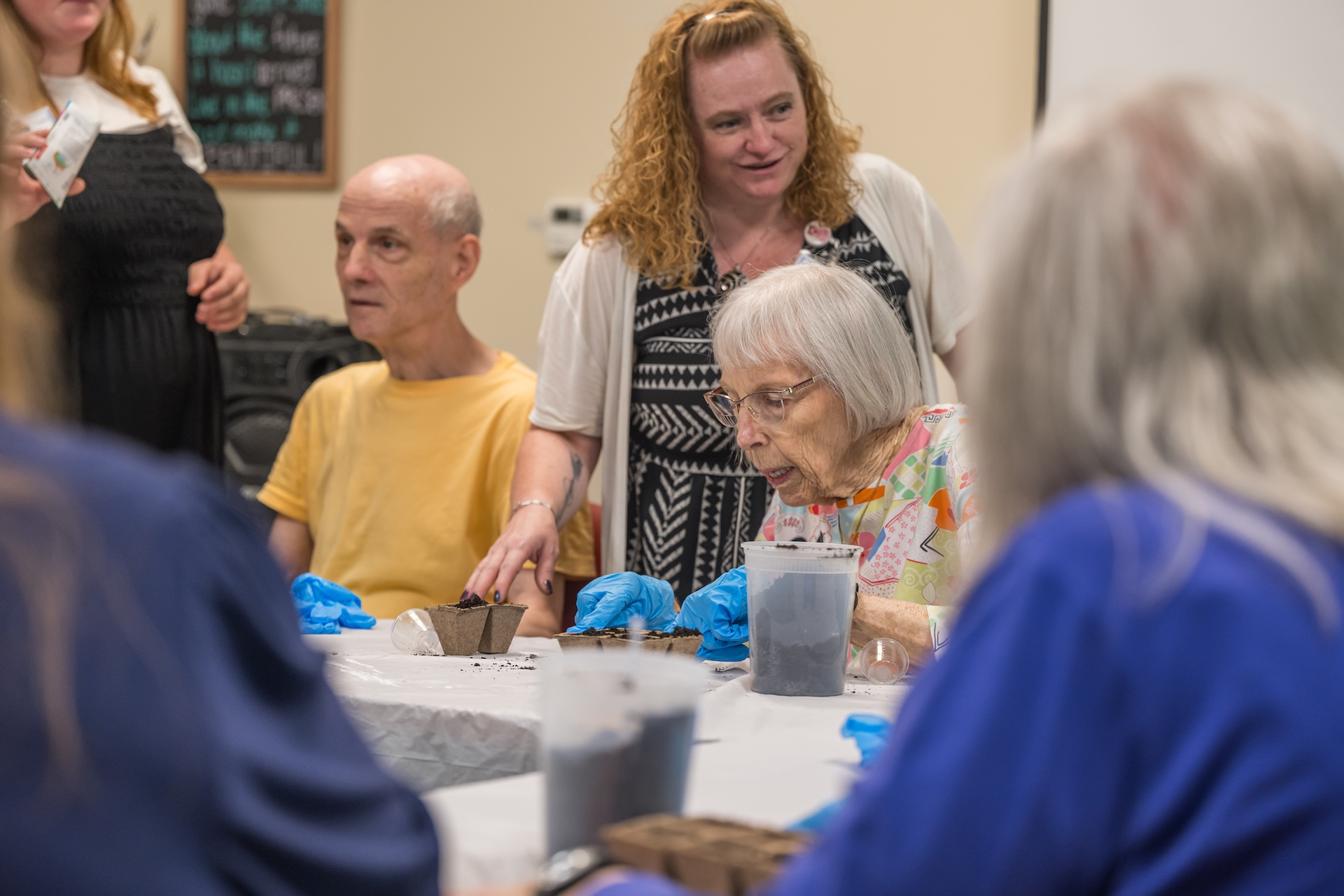 People at a table planting with a caregiver looking on.