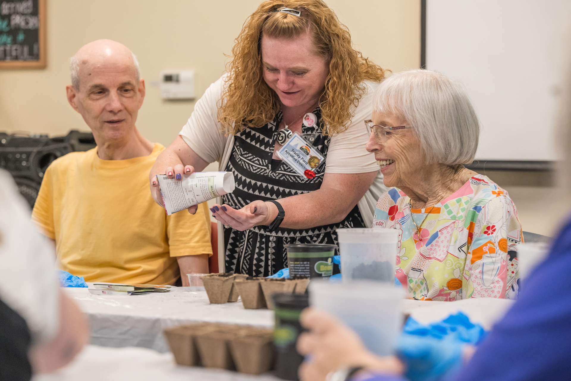 Woman assisting two people with planting seeds at a table. Indoor setting.