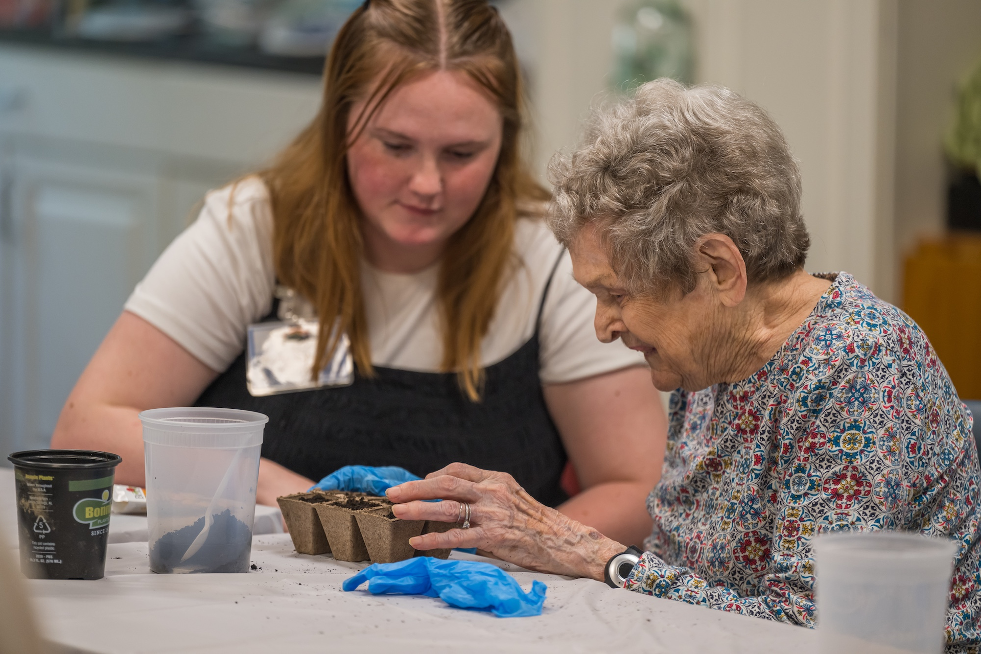 Woman and older adult planting seeds together at a table.