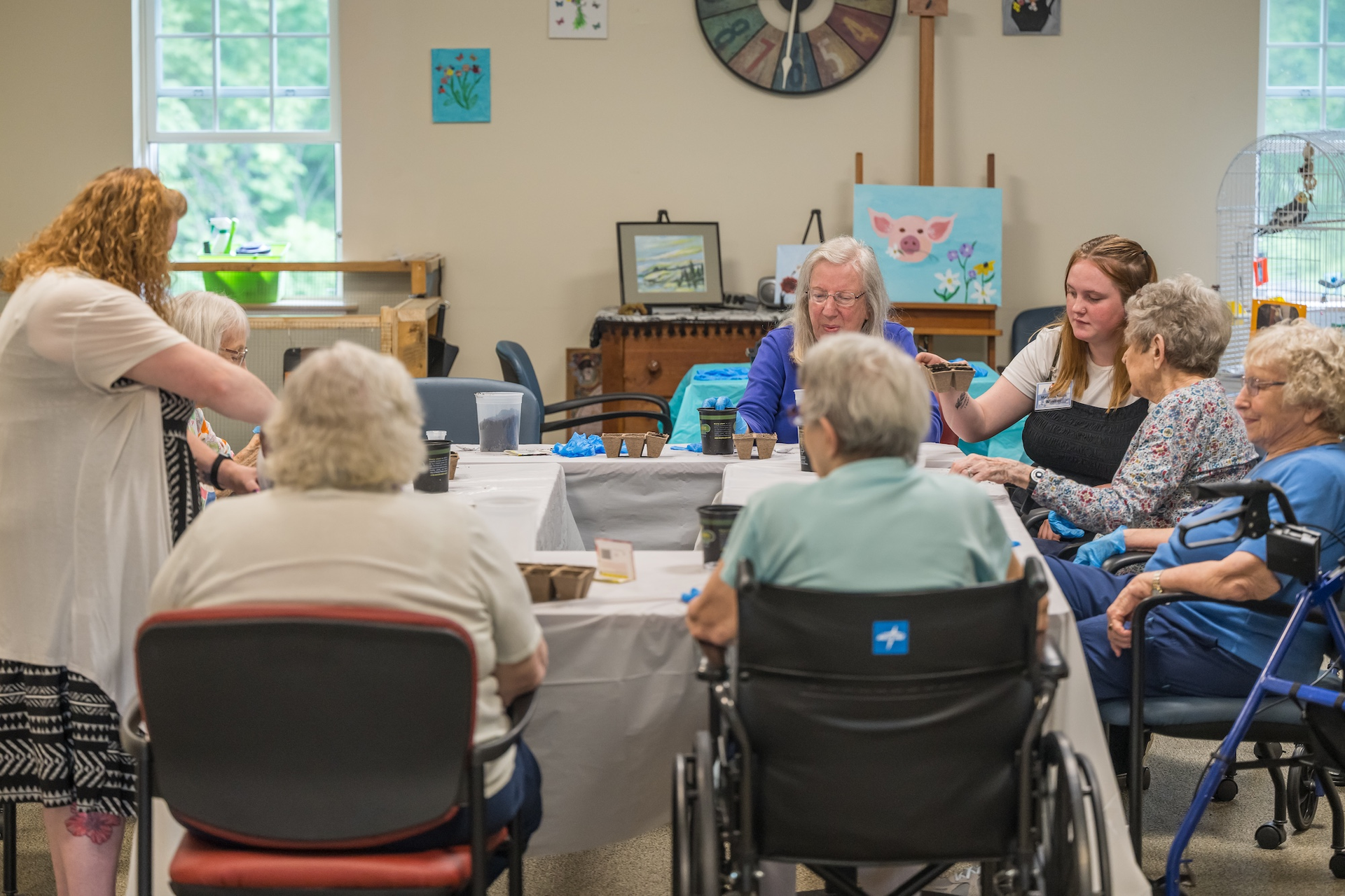 Seniors and staff seated around a table, participating in an activity in a brightly lit room.
