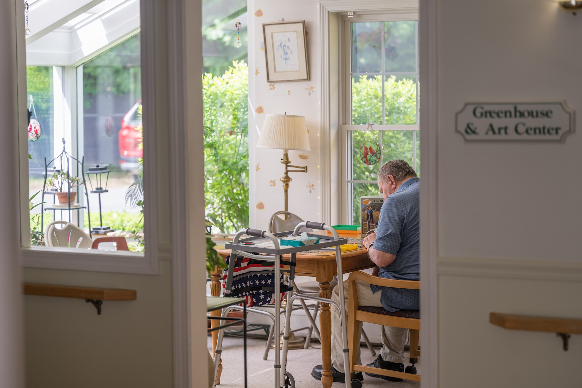 Man sitting at a table in a greenhouse art center, working on a project. Walker nearby.