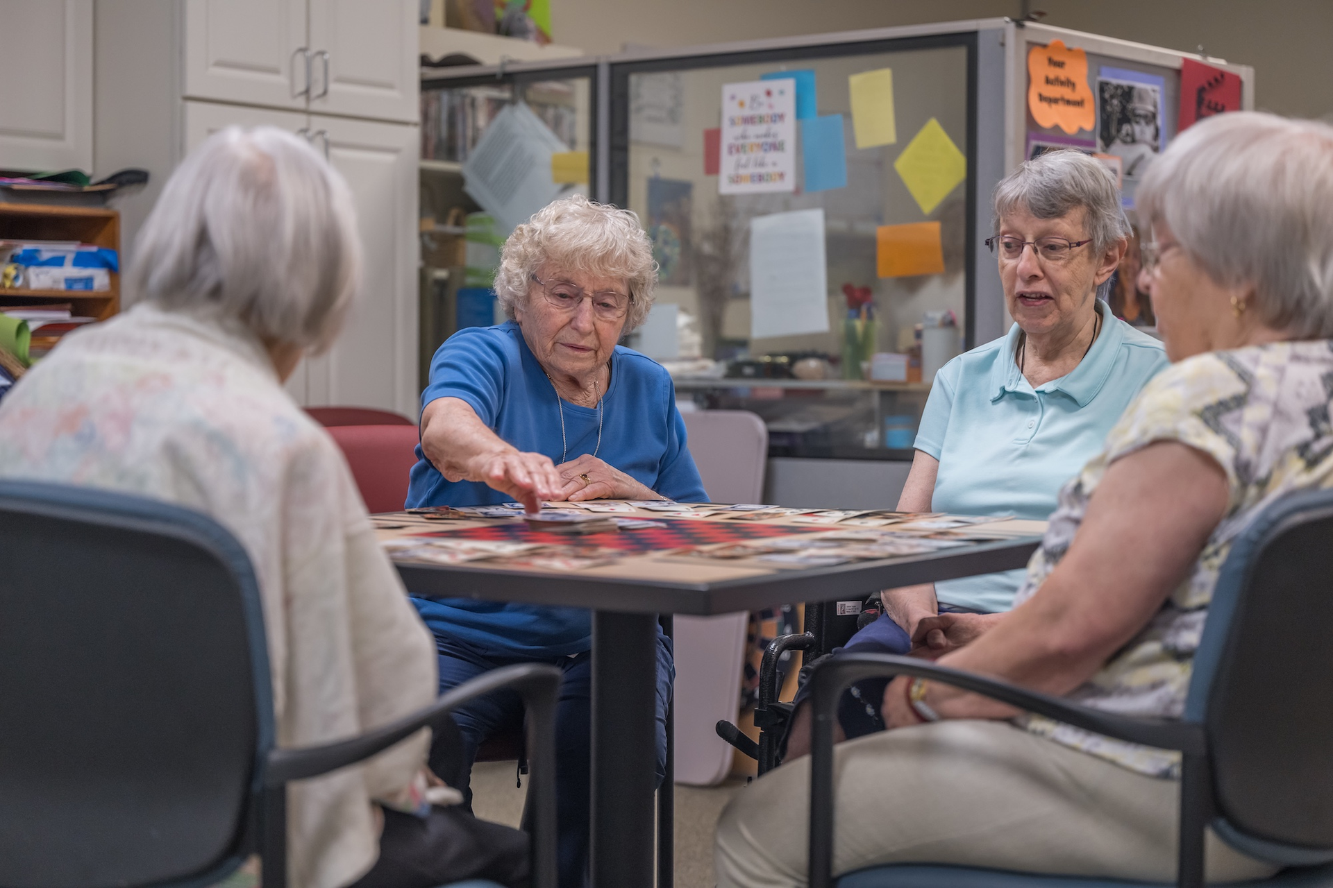 Four older adults seated at a table, working on a puzzle in a community room.