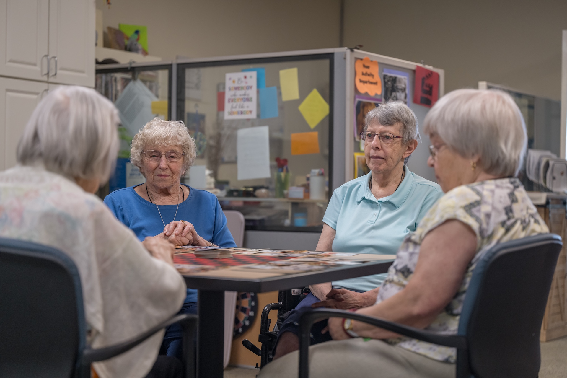 Four women seated at a table. They are playing a card game, in an indoor setting.