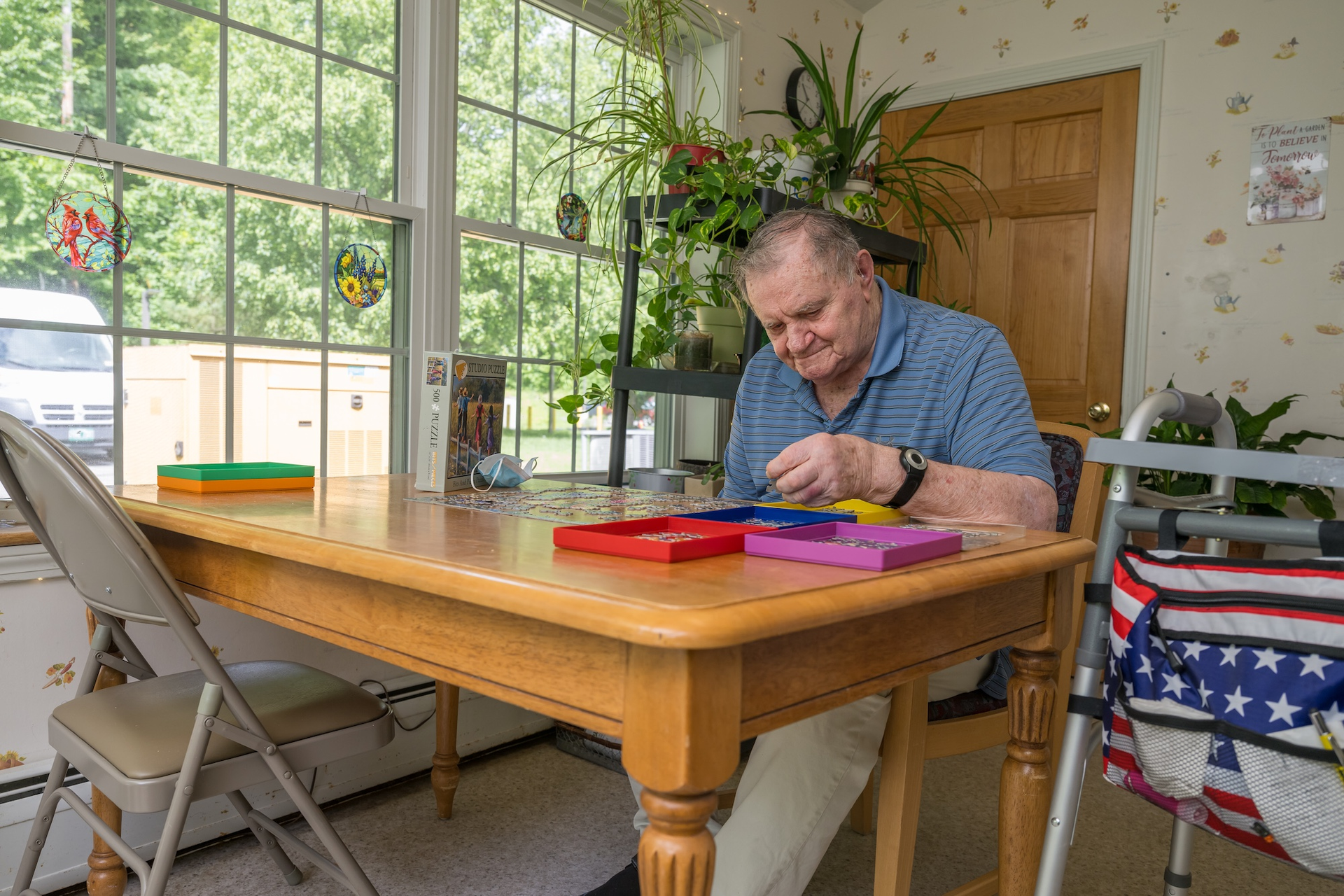 Man seated at table, crafting with colorful objects. Sunlight streams through window.