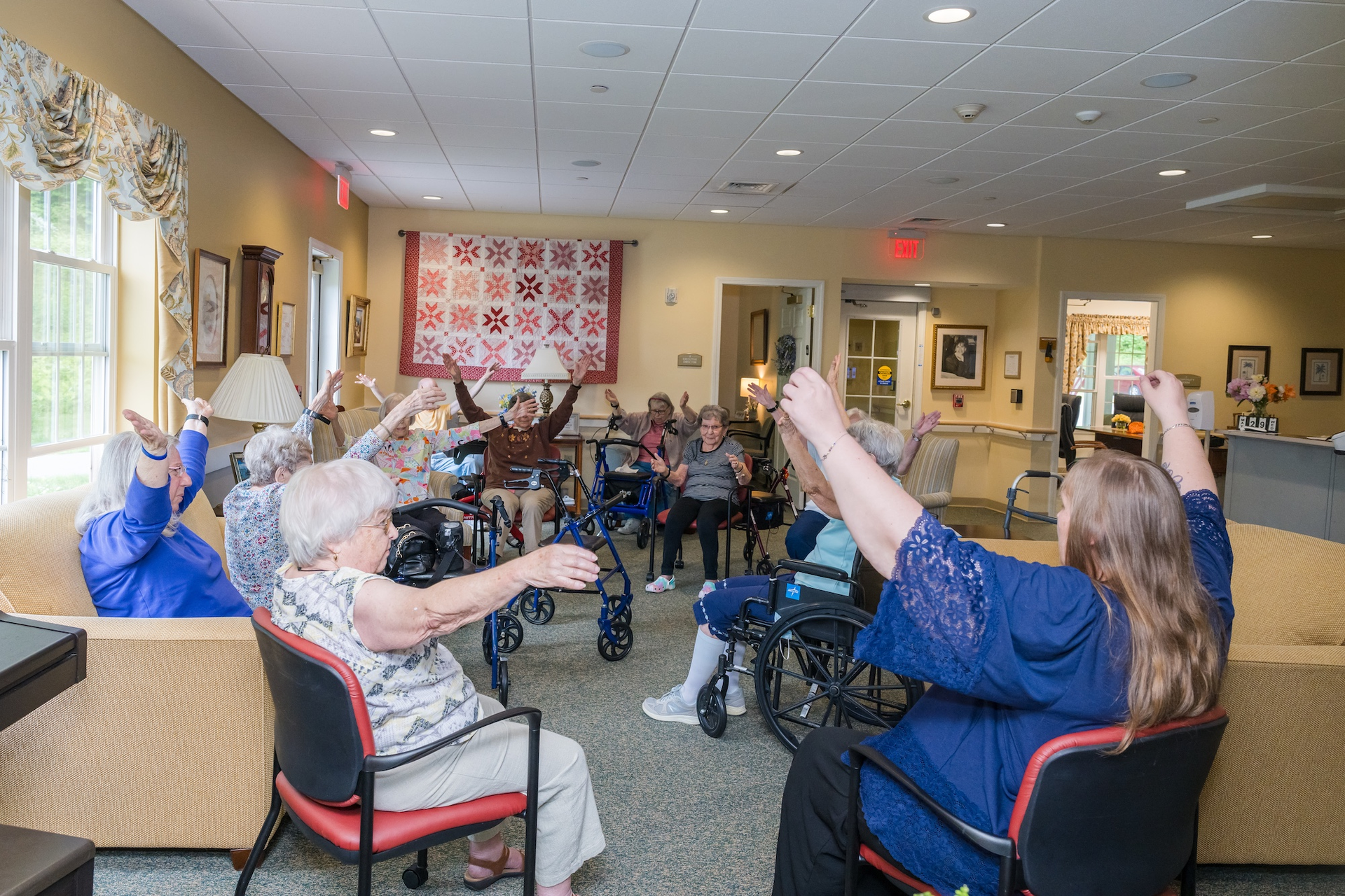 Group of seniors doing seated exercises in a community room with arms raised.