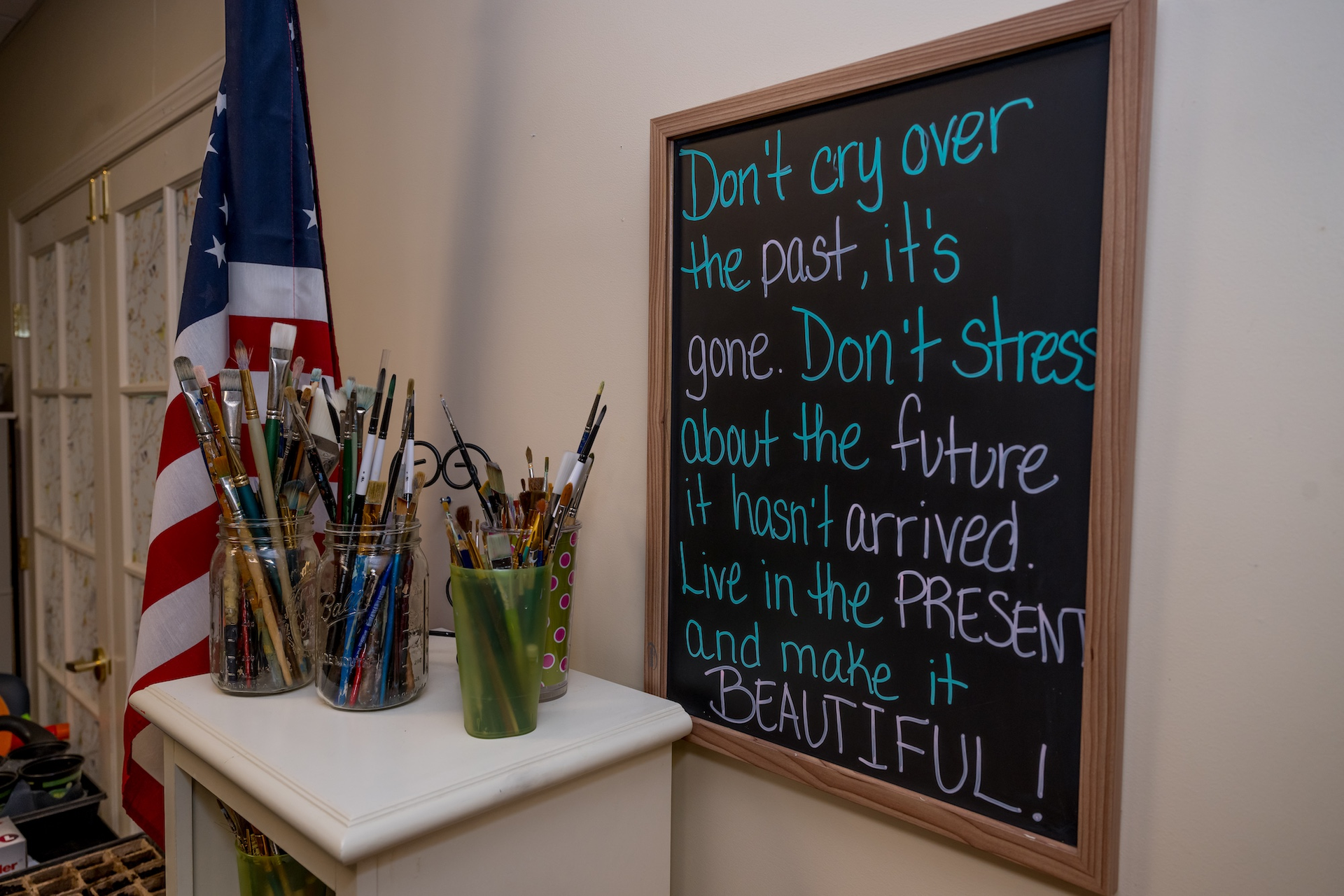 A chalkboard with a quote next to paint brushes, American flag and cabinet.