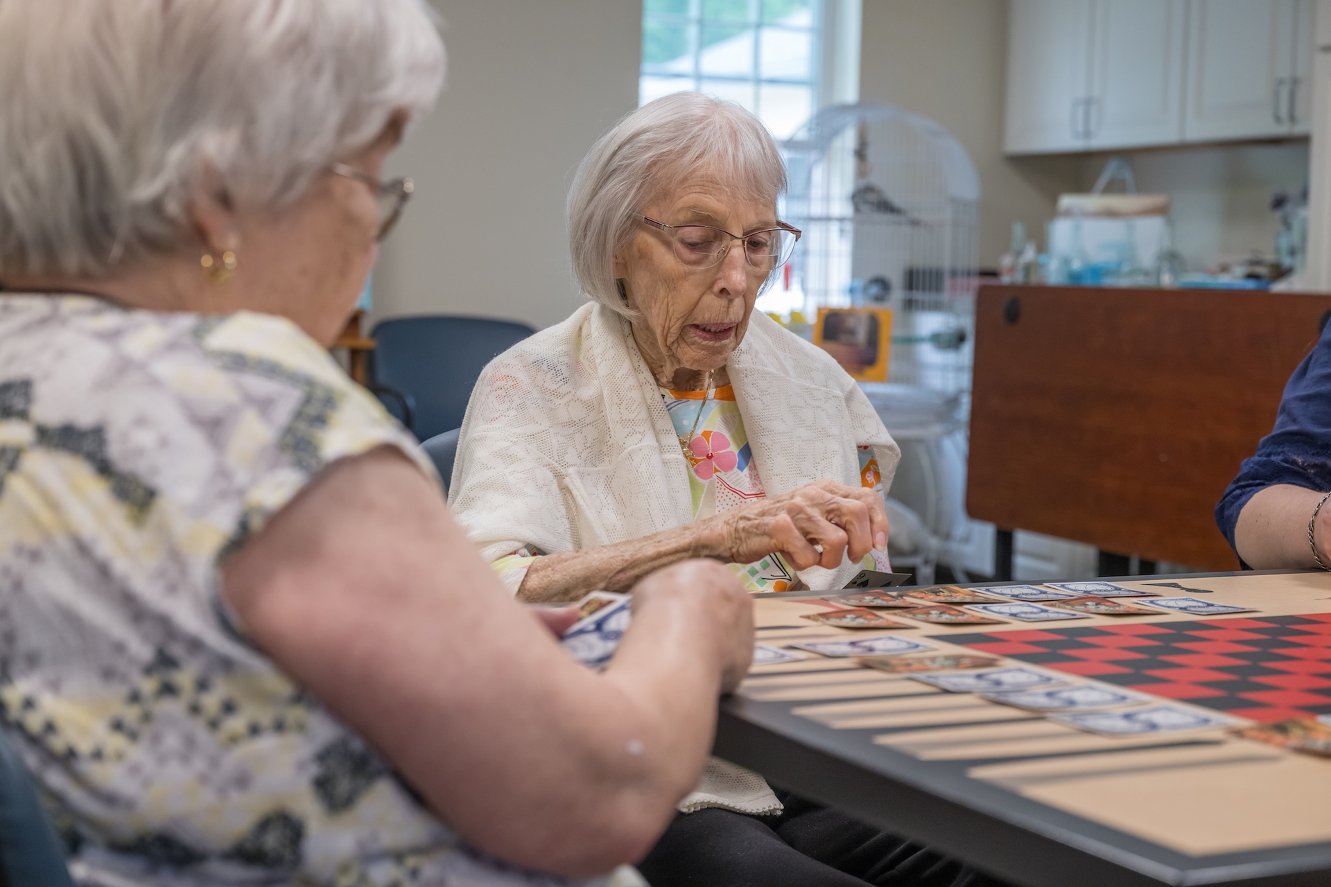 Two older adults playing a board game at a table indoors.