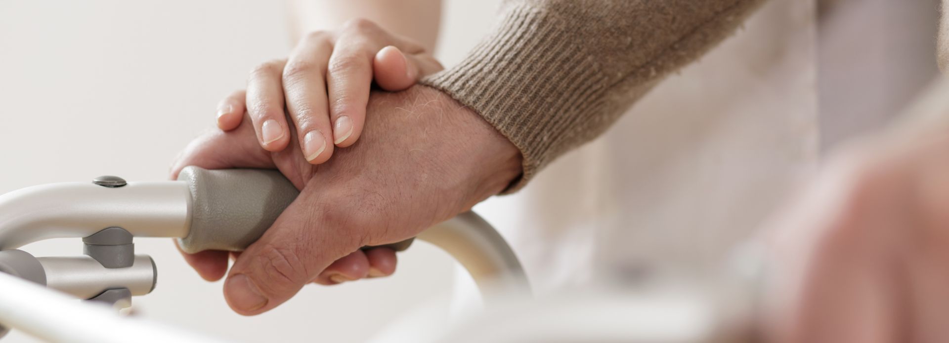 Person's hand on a walker is being held by another person's hand, offering support.