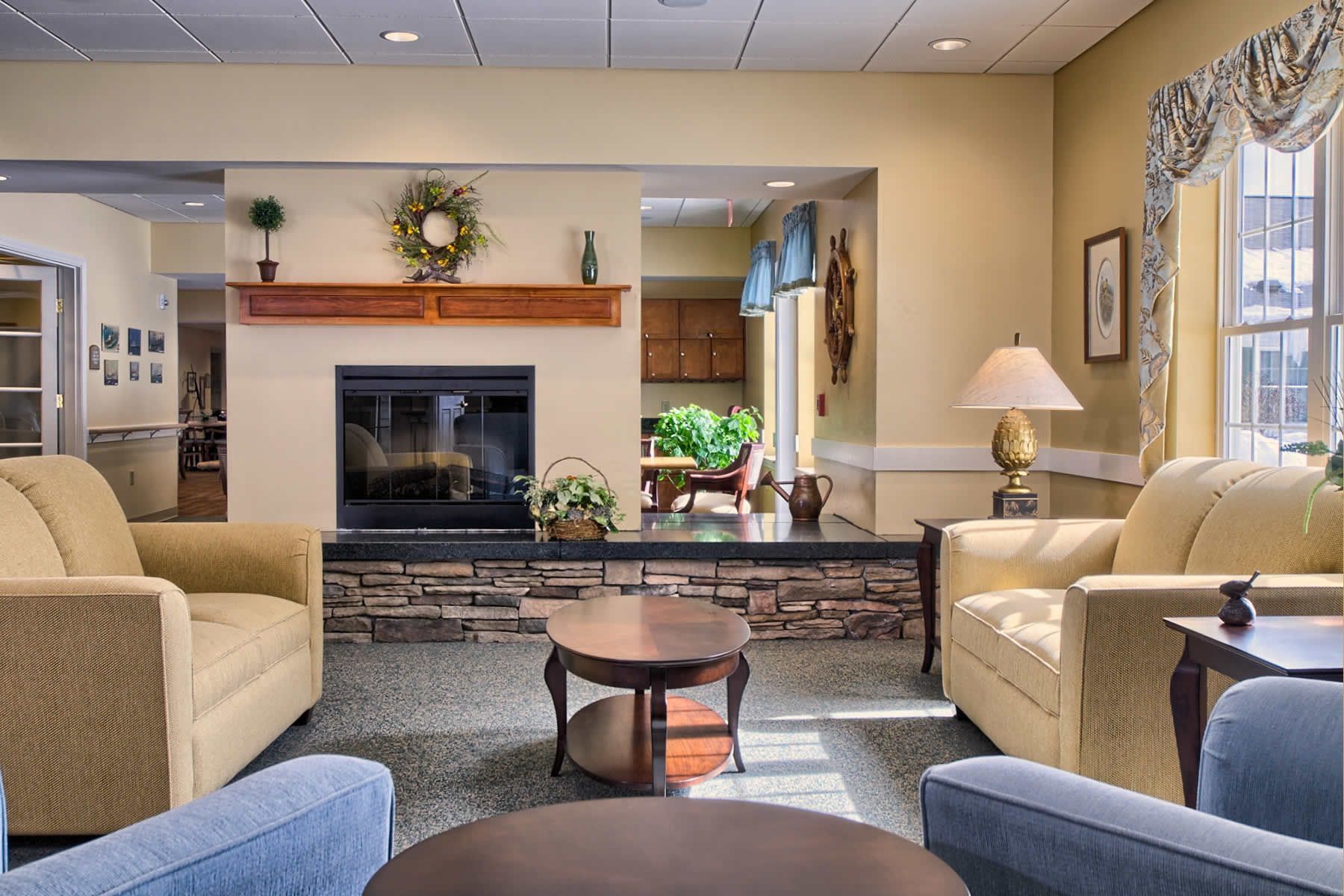 Cozy living room with yellow couches, fireplace, and side tables; window with floral valance; neutral tones.