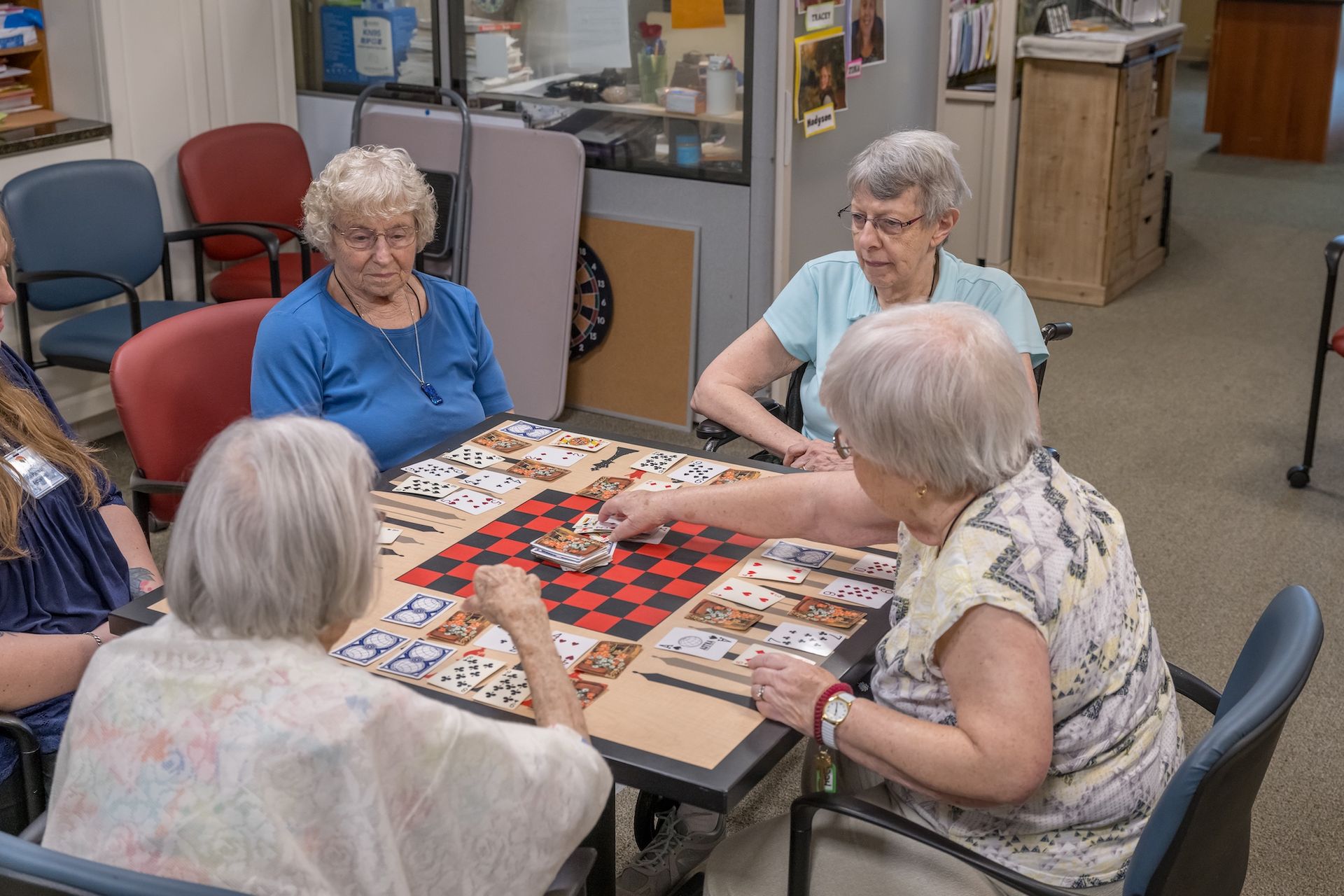 Four people play checkers at a table in a community room.