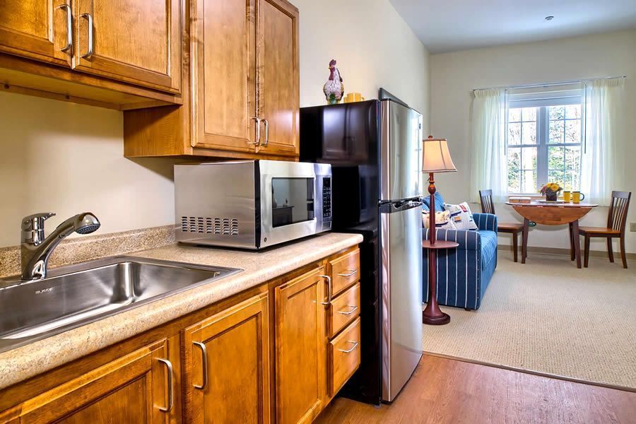 Small kitchen with microwave, fridge, and cabinets, opening to a living area with a sofa and dining table.