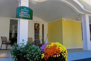 Entrance to a memory care center with a colorful floral display, under a white-columned porch.