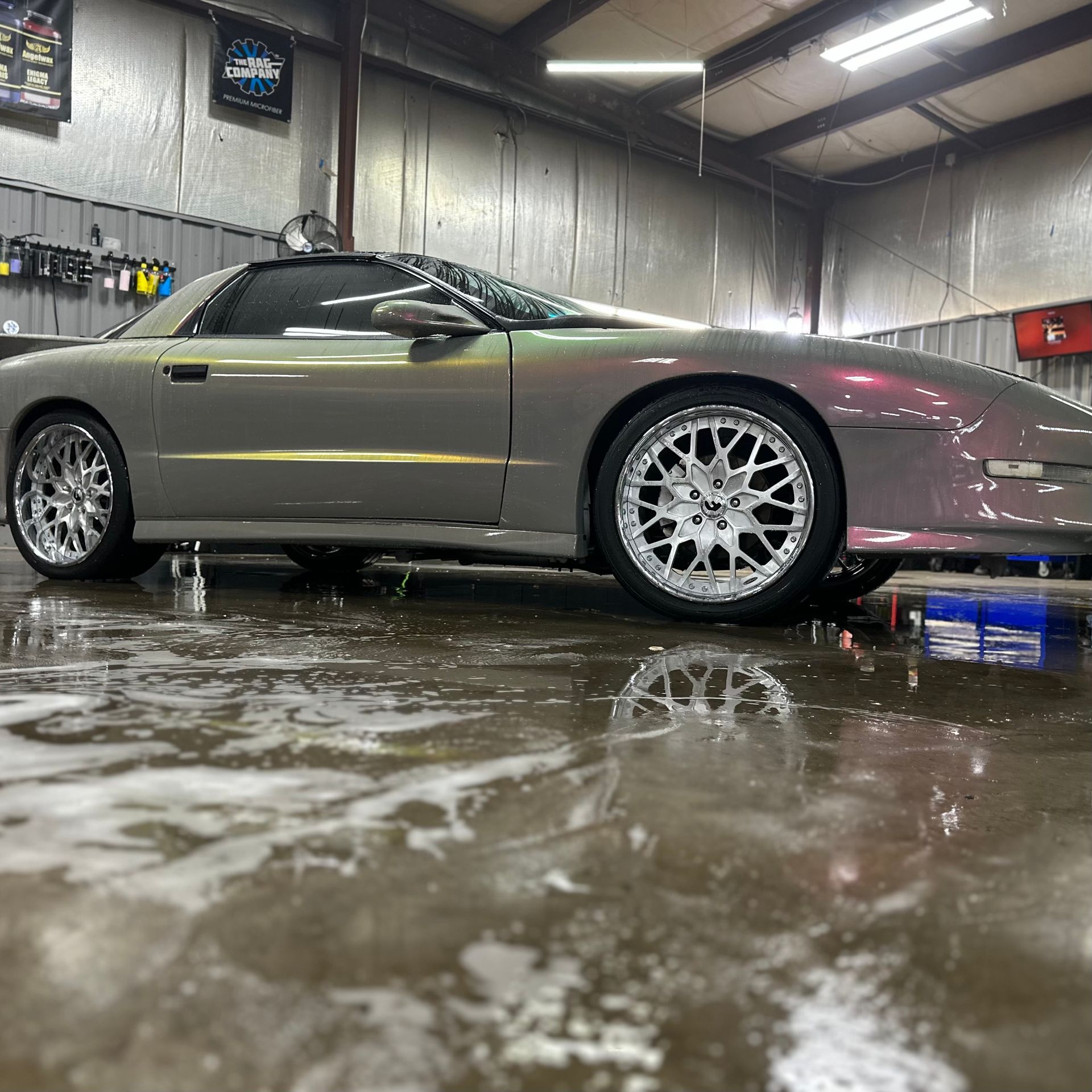 Silver sports car in a wet garage, shown in side profile with white wheels and reflections on the floor