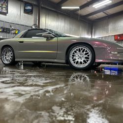 Silver sports car in a wet garage, shown in side profile with white wheels and reflections on the floor