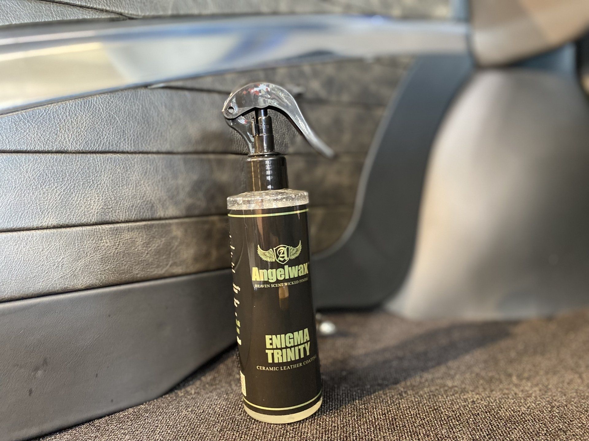Black spray bottle with yellow label on a car seat, against a metallic background.