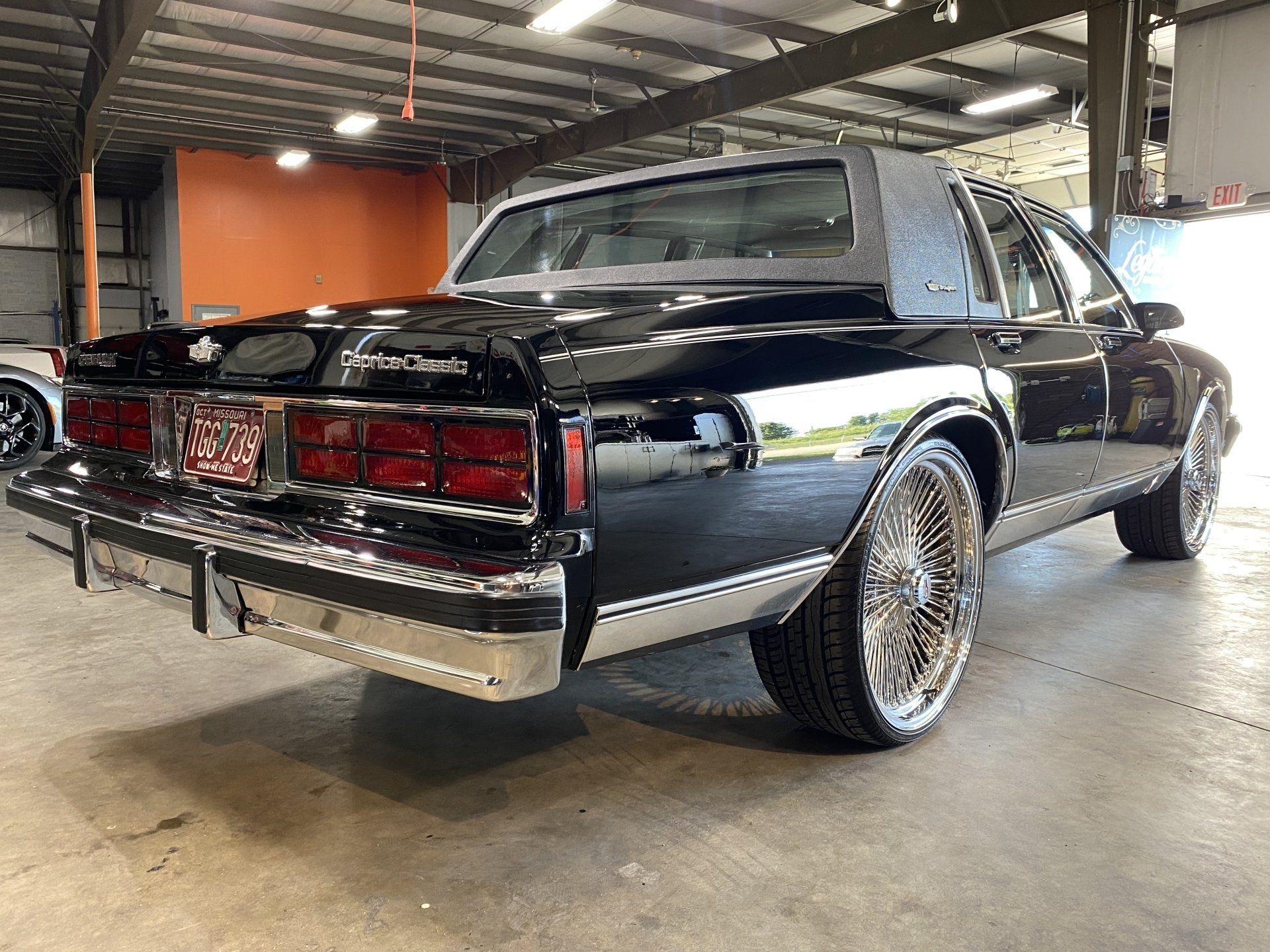 Classic black lowrider car with chrome trim parked indoors on a concrete floor.