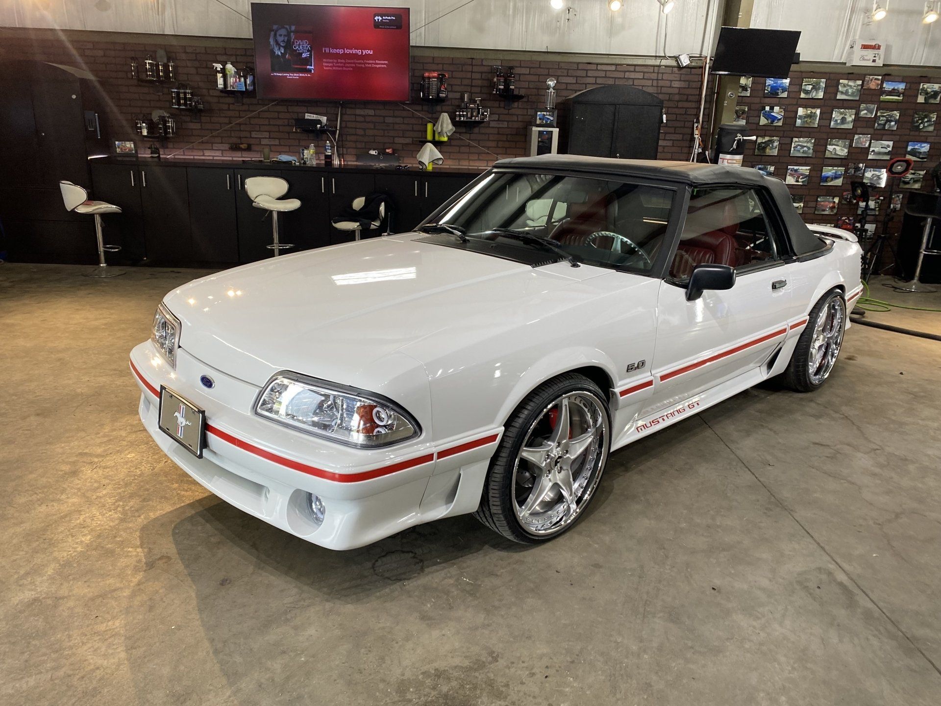 White sports coupe with red side stripe displayed indoors in a showroom