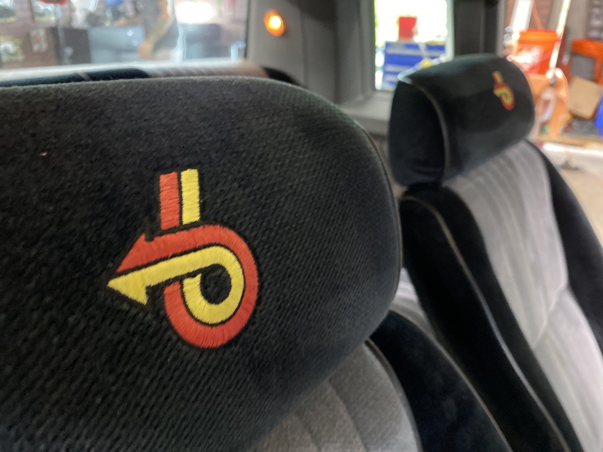 Close-up of a black car seat with a red and yellow logo on the headrest.