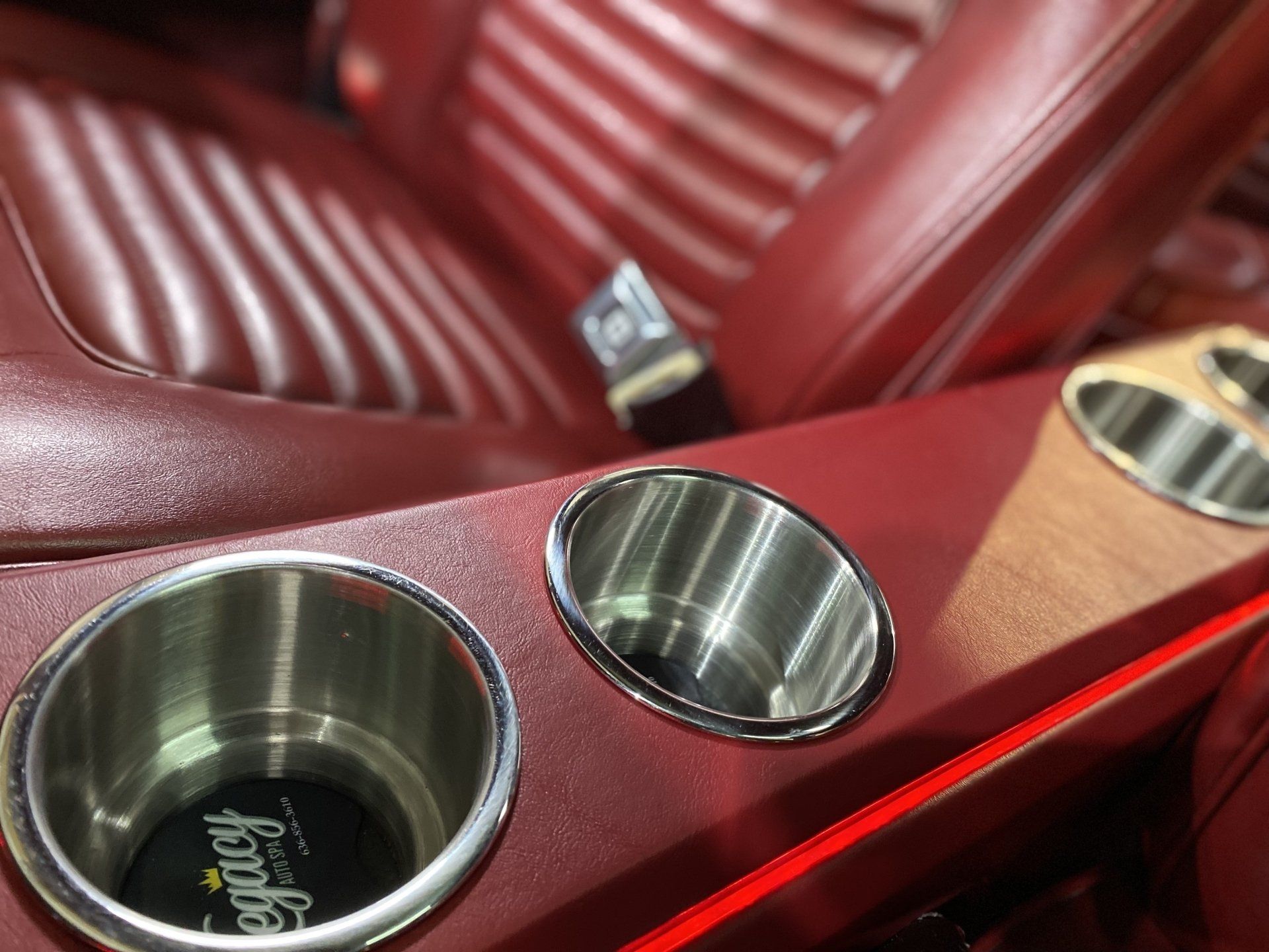 Red leather car seat with a wooden console holding two stainless steel cup holders