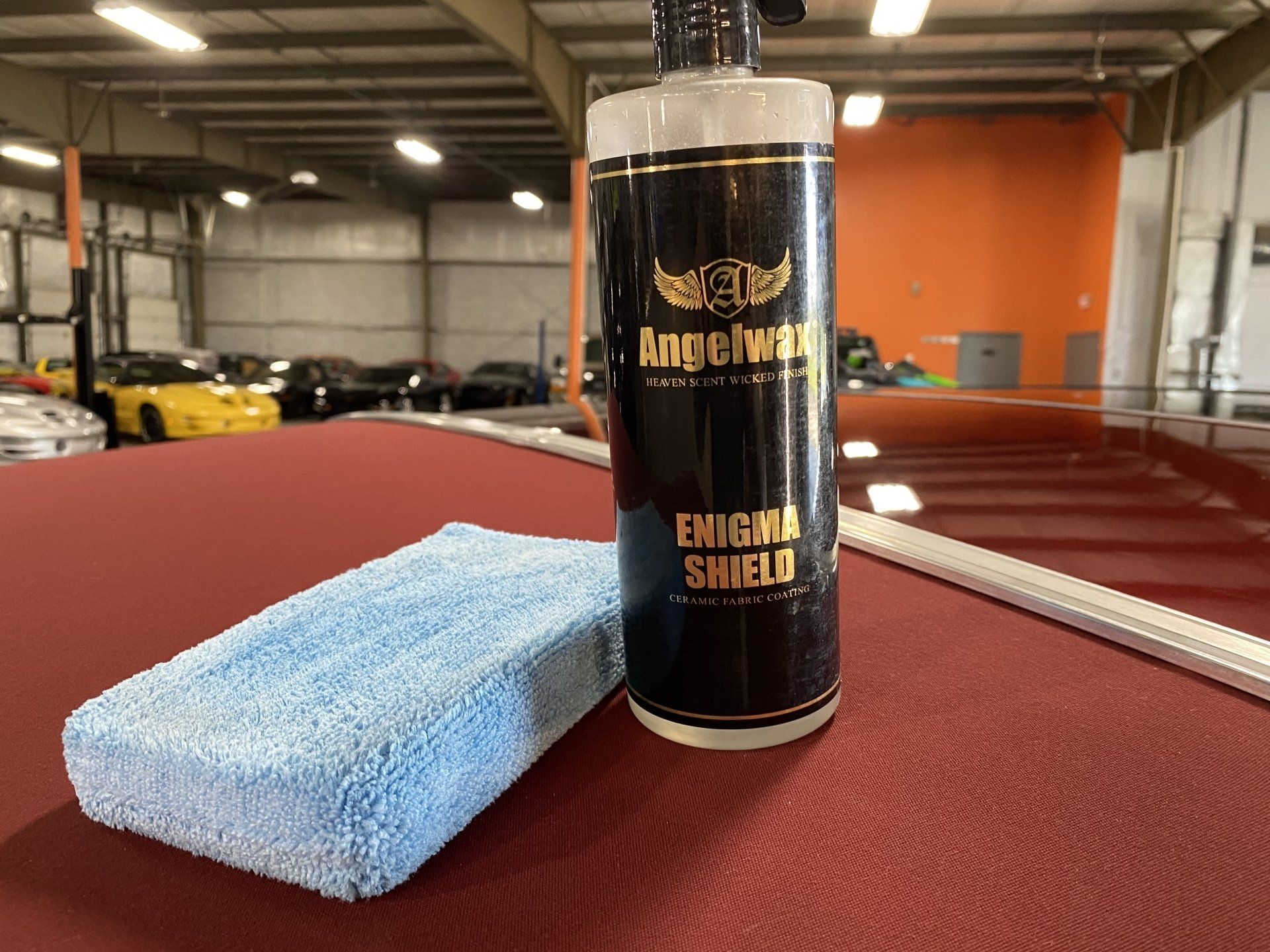 Car detailing spray bottle beside a blue microfiber applicator on a red car seat in a garage