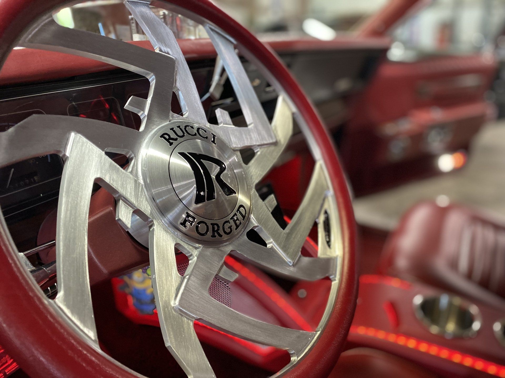 Close-up of a custom silver steering wheel in a red car interior with red leather seats and dashboard lights