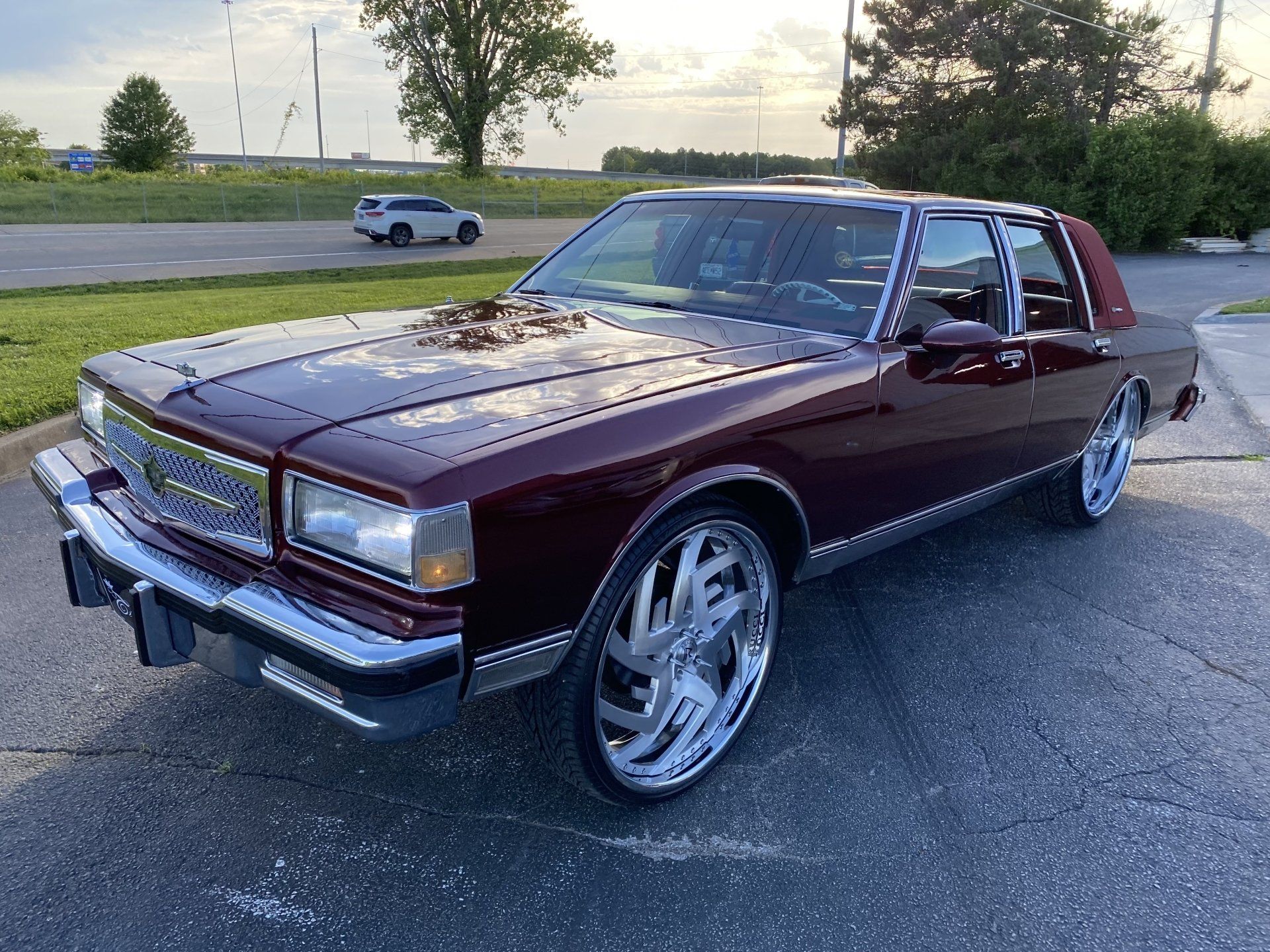 Maroon classic sedan with chrome rims parked on pavement at sunset