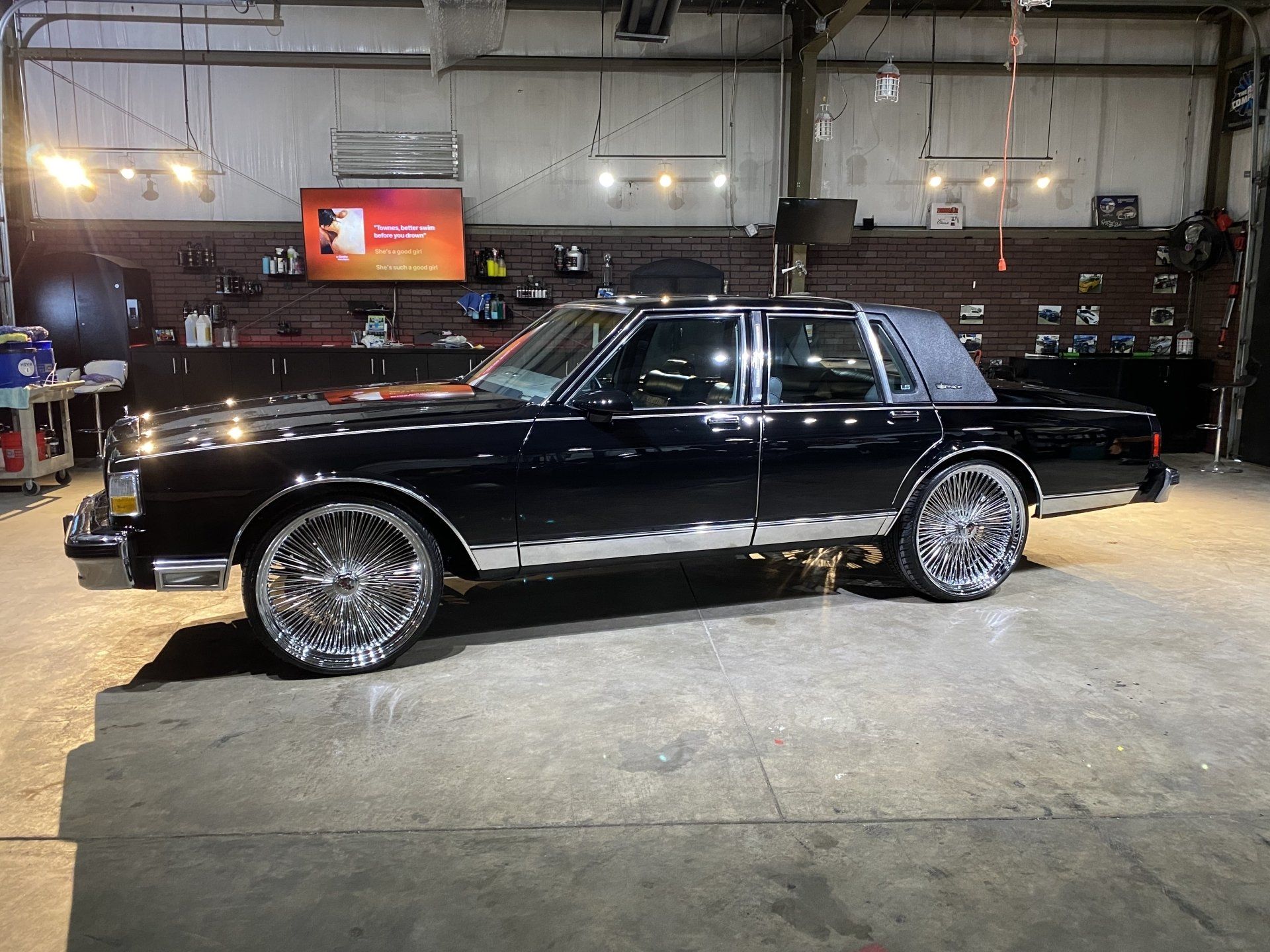 Black classic car with chrome rims parked indoors in a garage or showroom