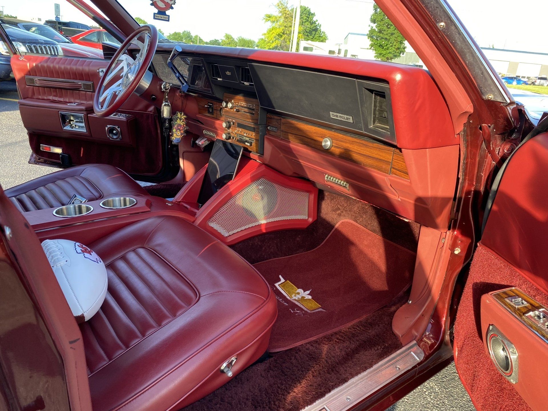 Red vintage car interior with maroon leather seats and dashboard, viewed from the open passenger door
