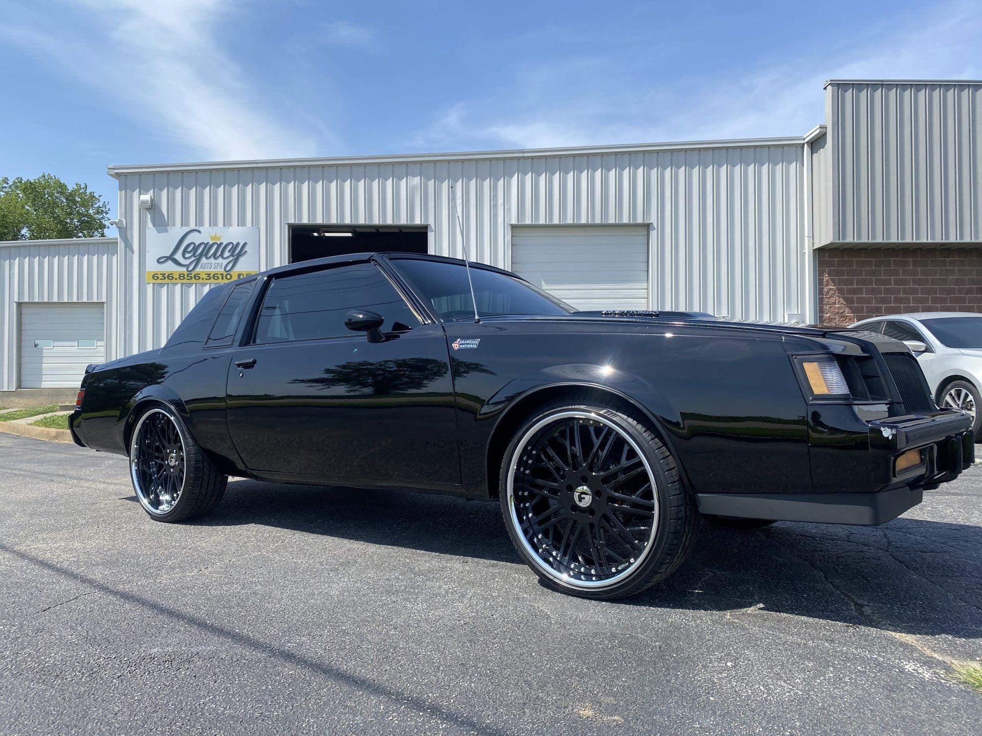 Black classic coupe parked outside a metal building under a blue sky.