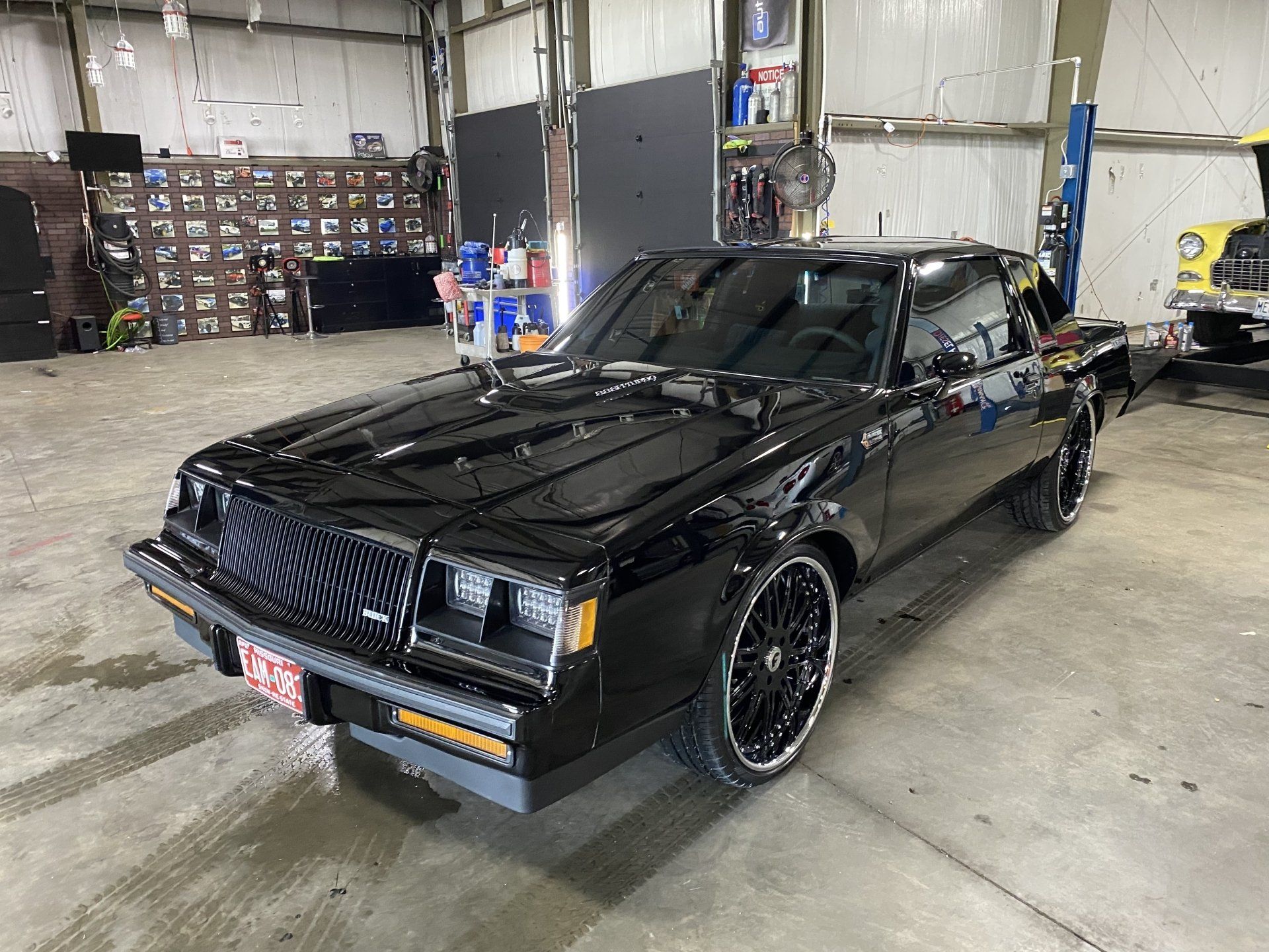Black classic coupe parked in a garage, front-left view, with glossy paint and chrome trim