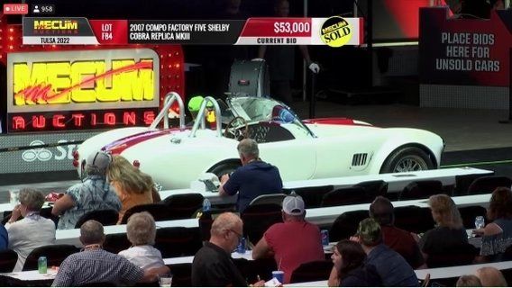 White classic convertible on a live auction stage with bidders seated in front