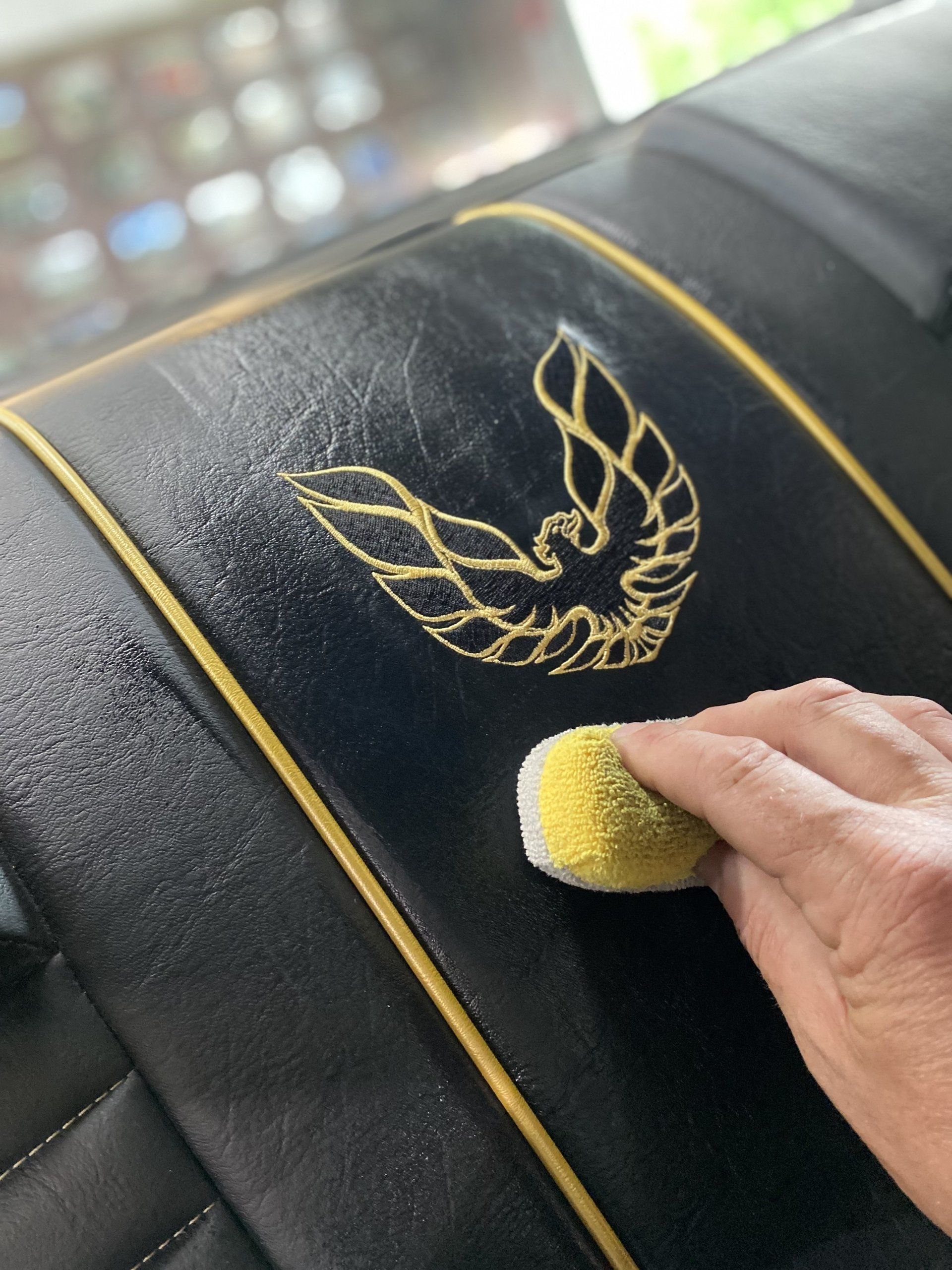Hand cleaning a black leather seat with yellow trim and a gold embroidered logo