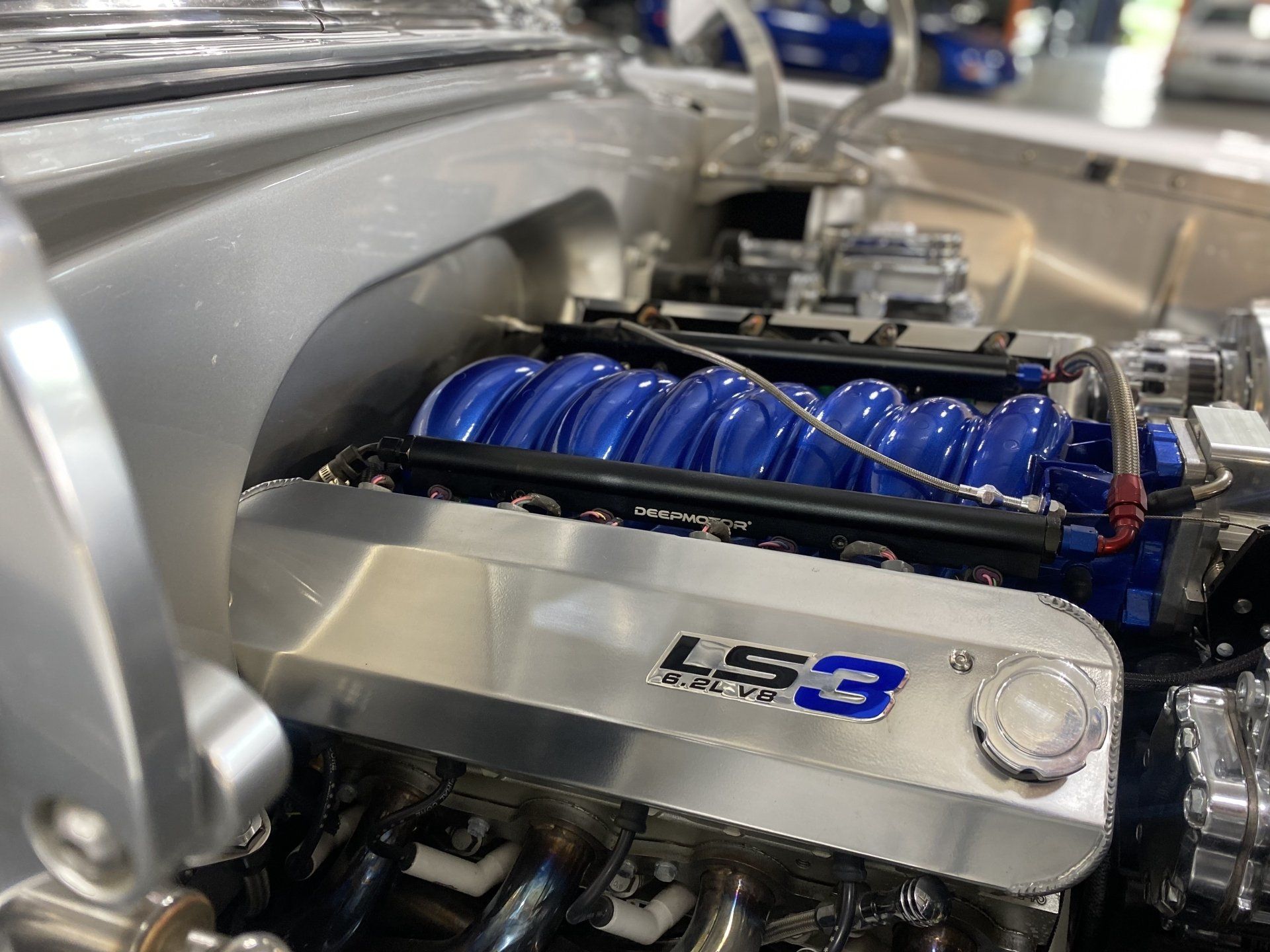 Close-up of a polished LS3 car engine with blue intake manifold tubing and chrome components