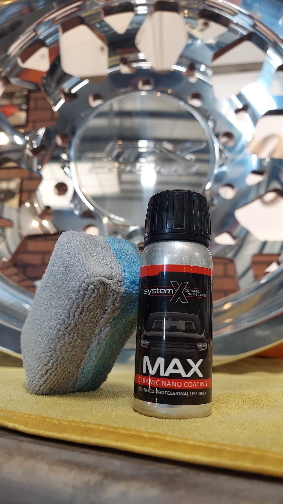 Small black bottle labeled “MAX” beside a gray foam block on a table, with a reflective metal wheel in the background