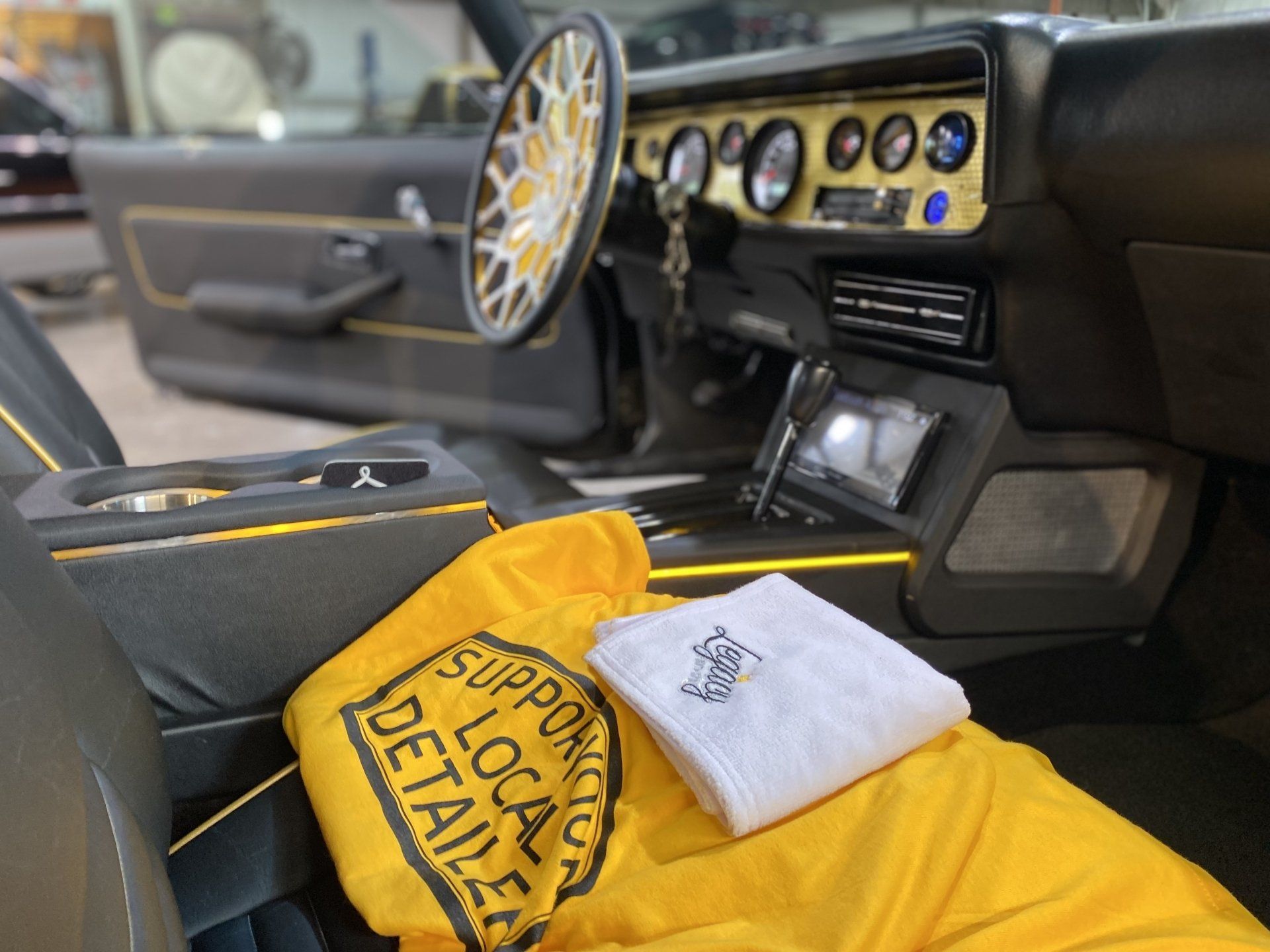 Car interior with black and yellow custom seats, dashboard gauges, and a yellow tote bag on the passenger seat