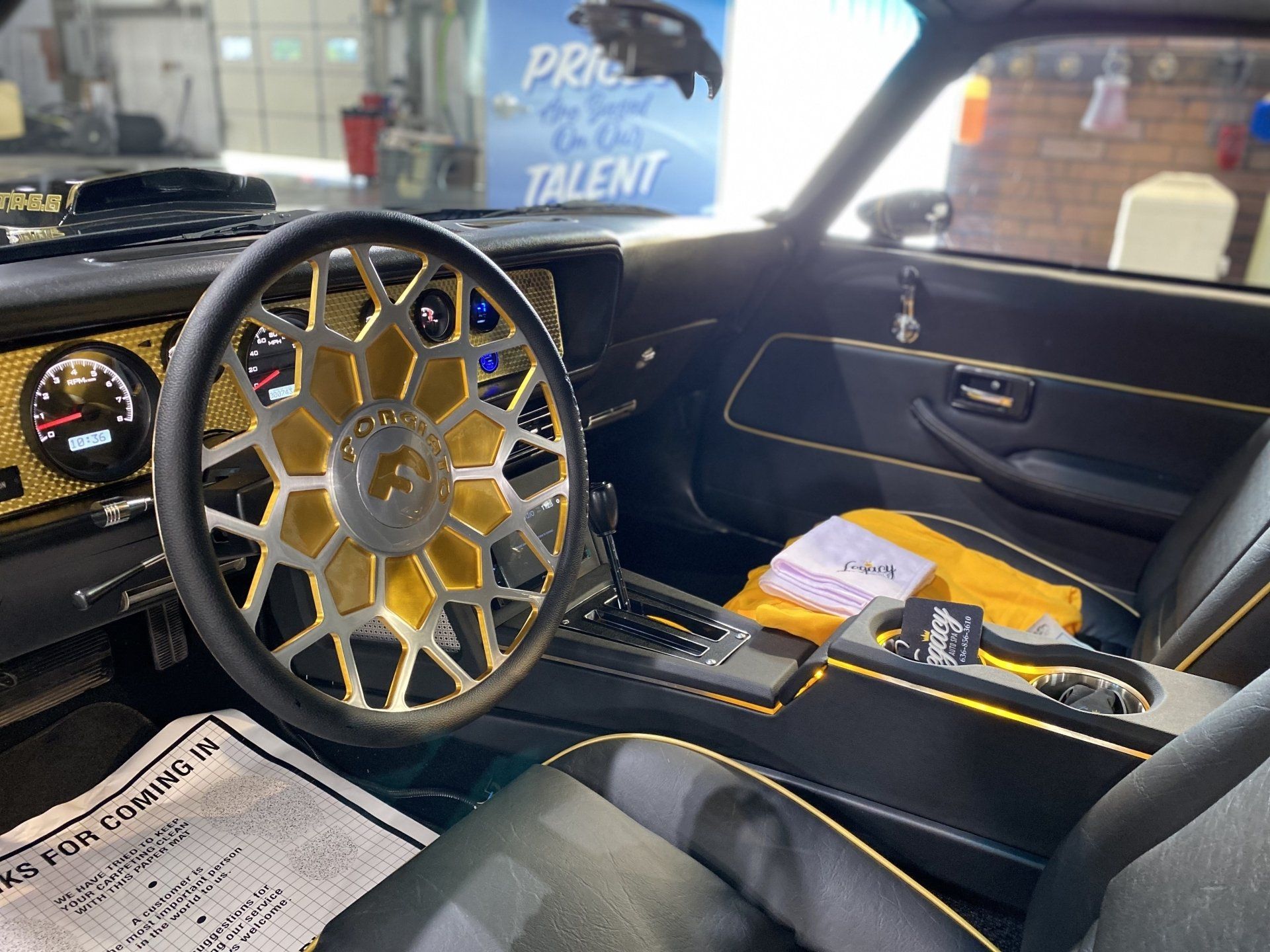 Custom car interior with a gold-and-chrome steering wheel and black dashboard, viewed from the driver’s seat