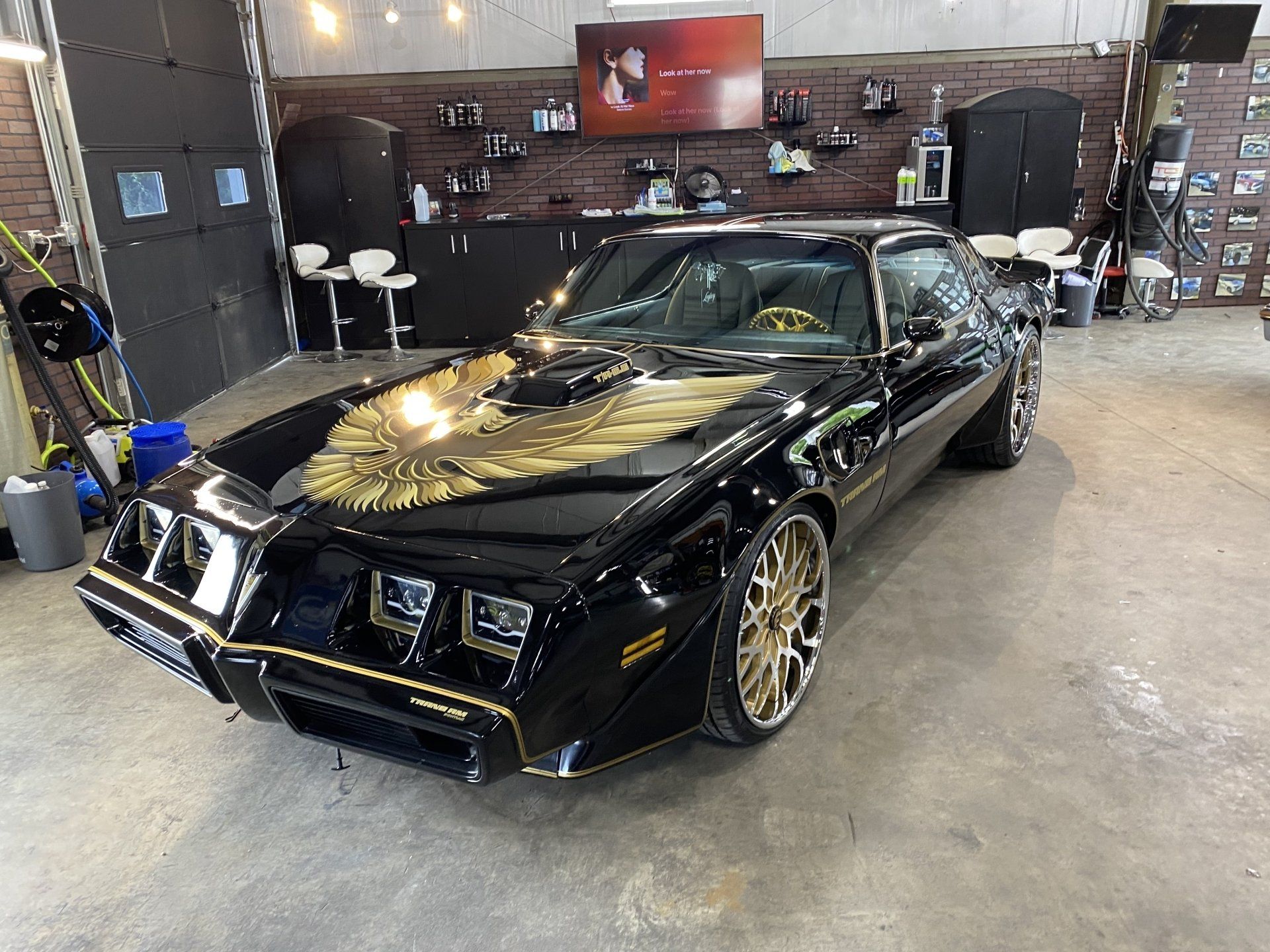 Black classic muscle car on display indoors with gold wheels and custom front splitter