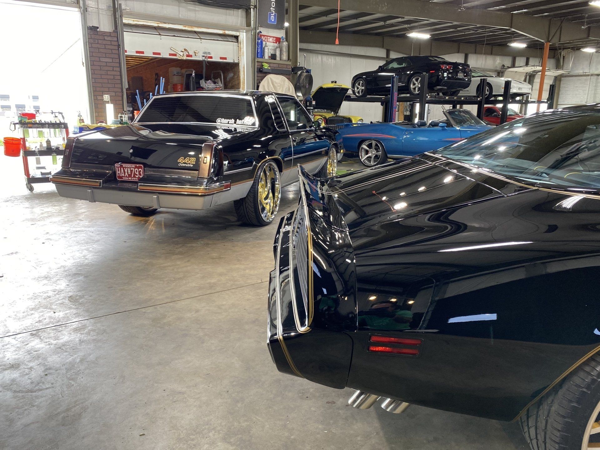 Classic cars in a garage, including a black convertible and a black coupe with blue accents