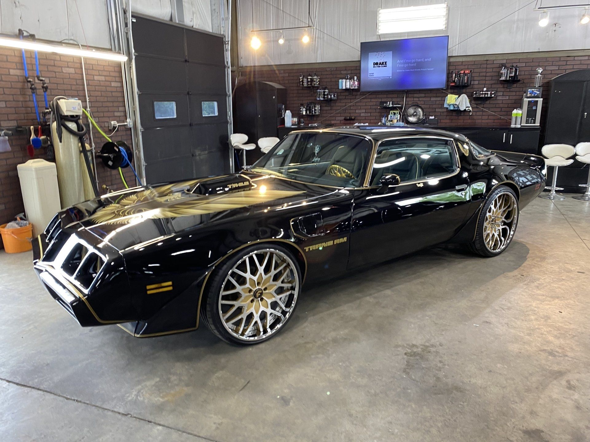 Black classic sports car with gold rims parked inside a garage.