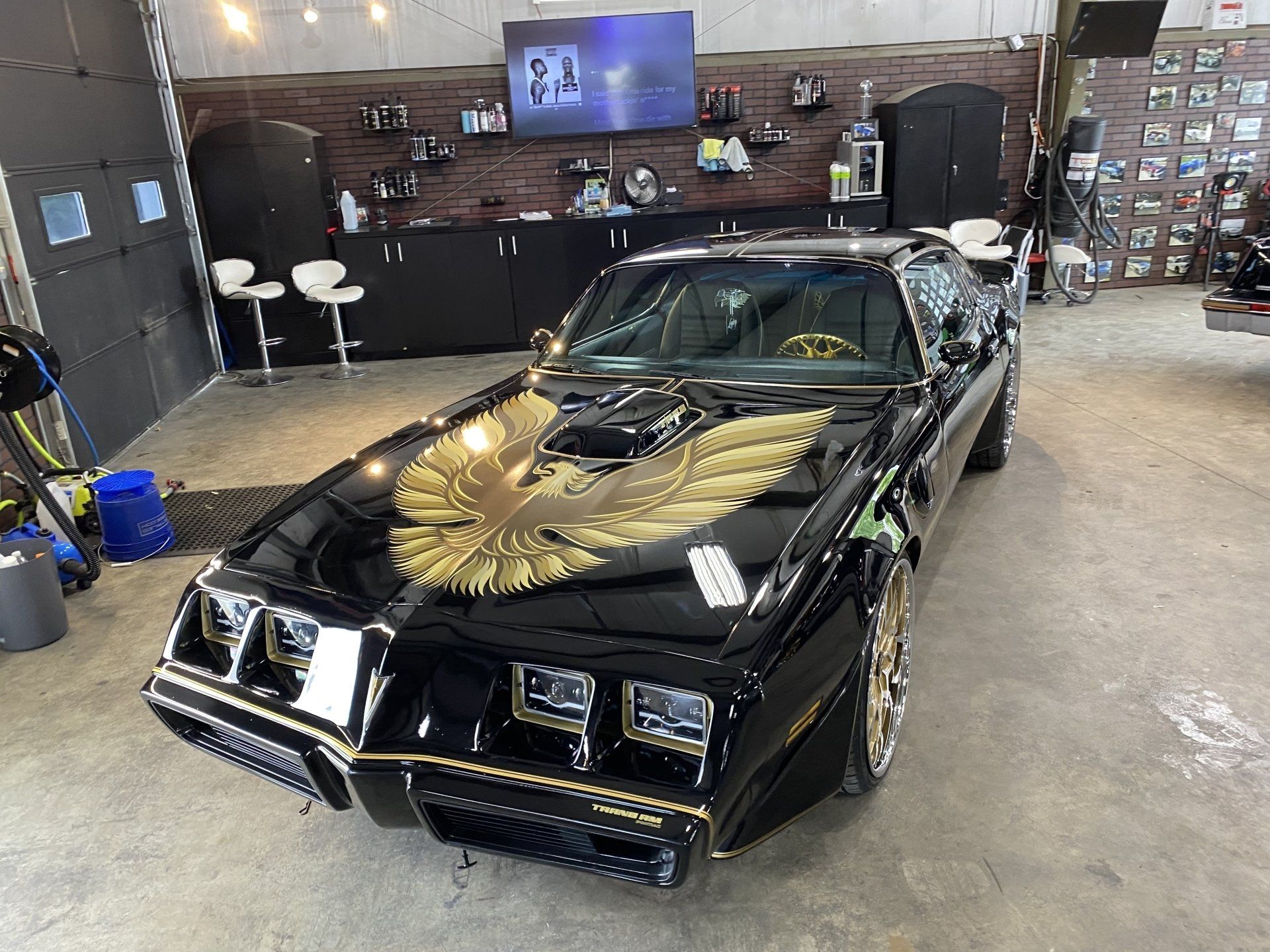 Black classic car with gold eagle hood decal in an auto shop garage