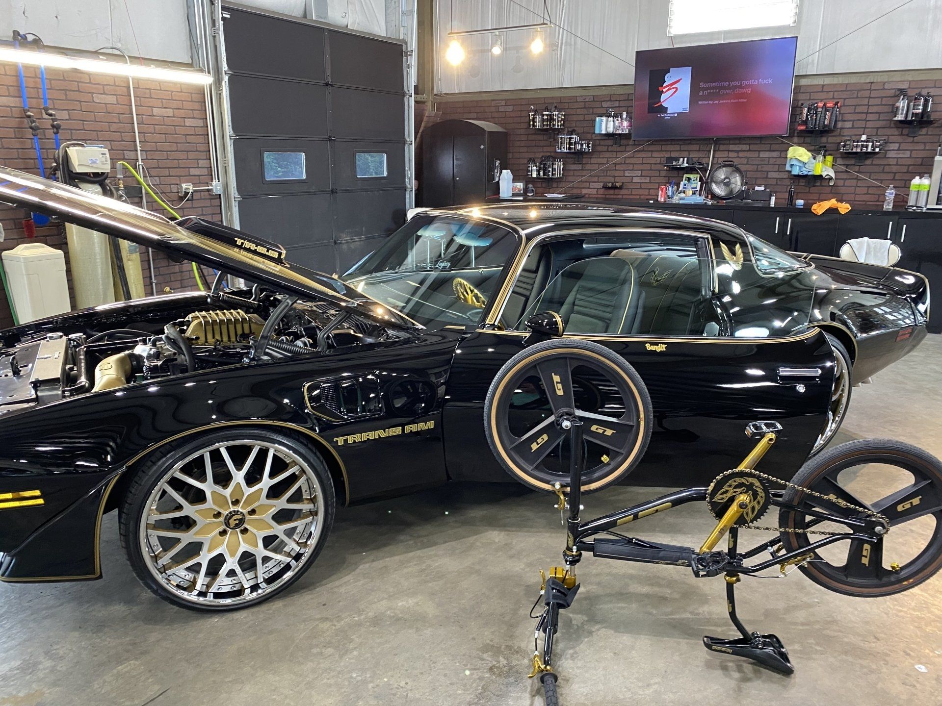Black sports car in a garage with a bicycle in the foreground and its hood open