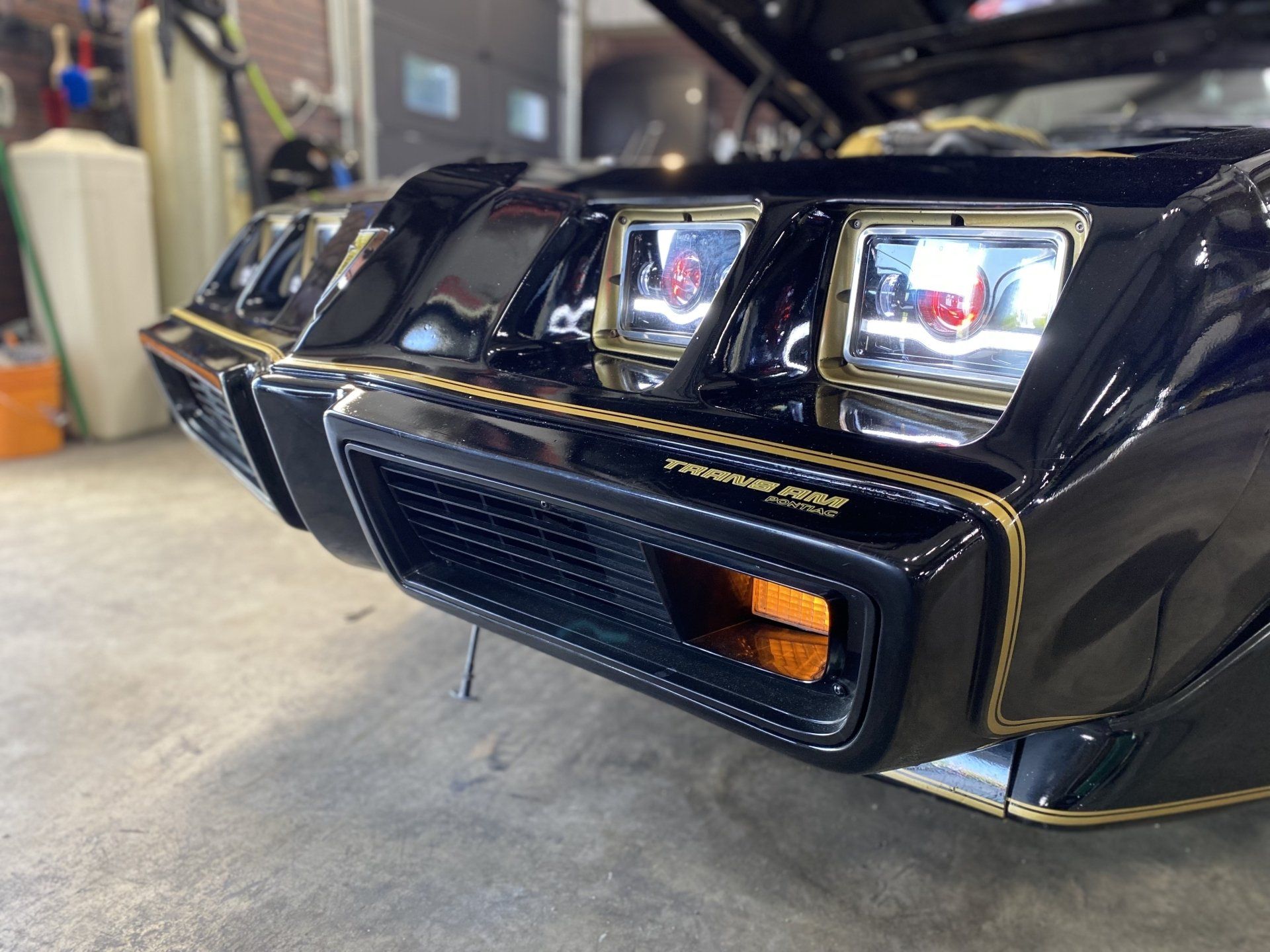 Black vintage sports car front end with quad headlights and orange turn signal in a garage