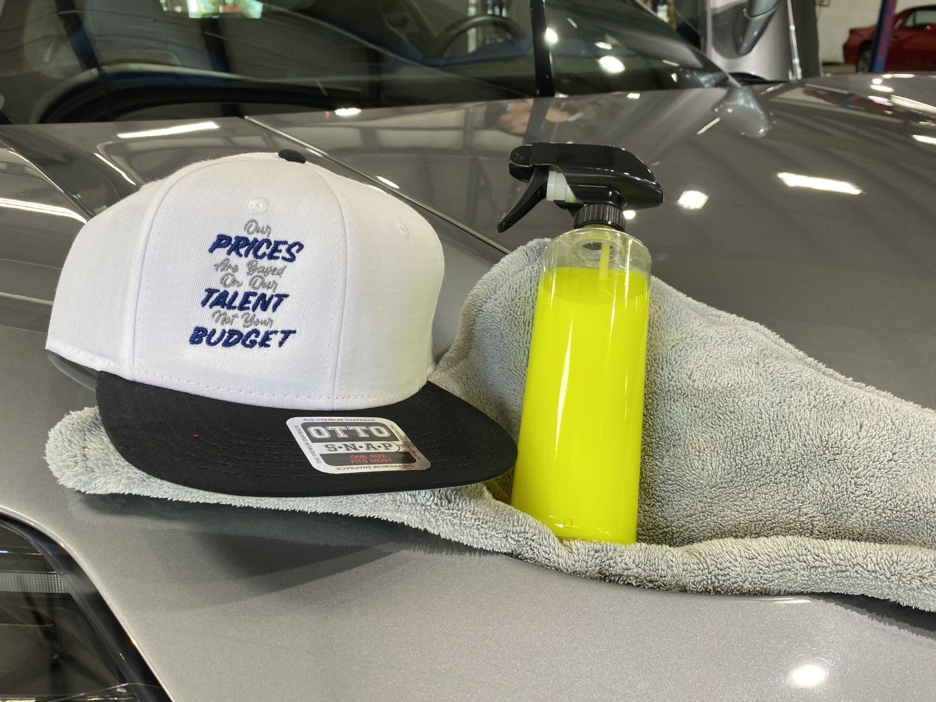 White-and-black trucker hat and neon yellow spray bottle on a gray microfiber towel inside a car interior