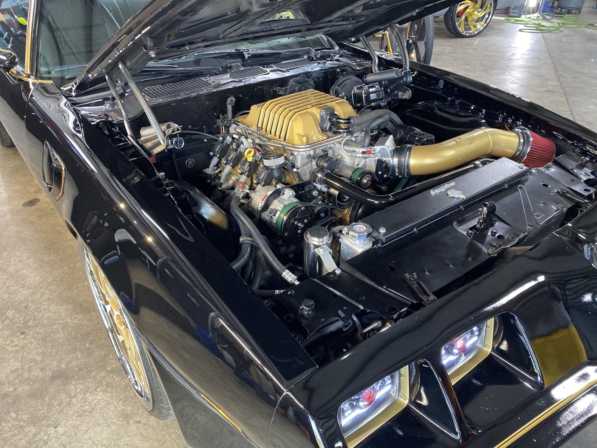 Black classic car with hood open, showing a modified engine and glossy custom front end.